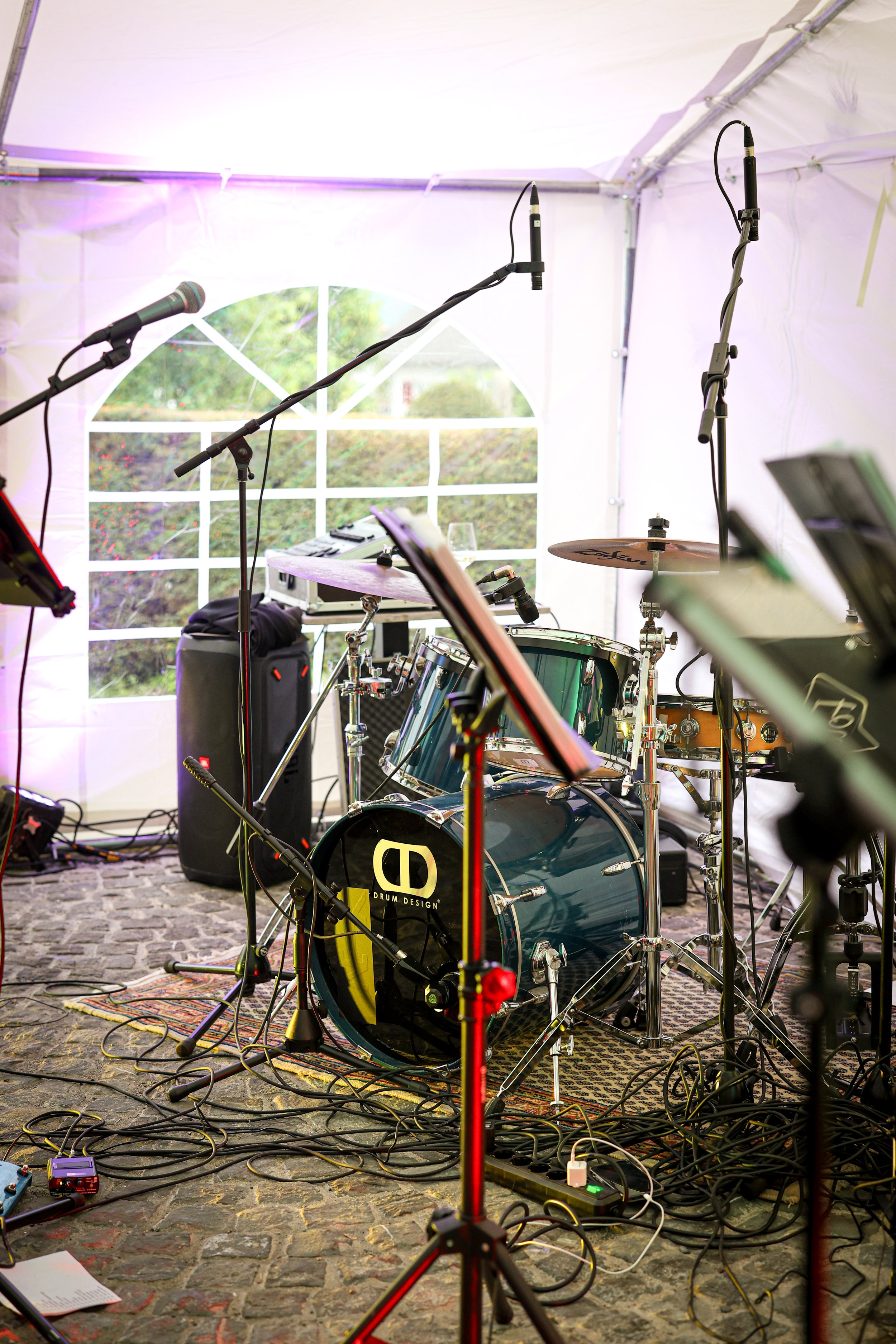 Musik-Bühne mit Schlagzeug, Mikrofonen, Kabeln und Equipment in einem Zelt, im Hintergrund ein Fenster mit Blick nach draußen.