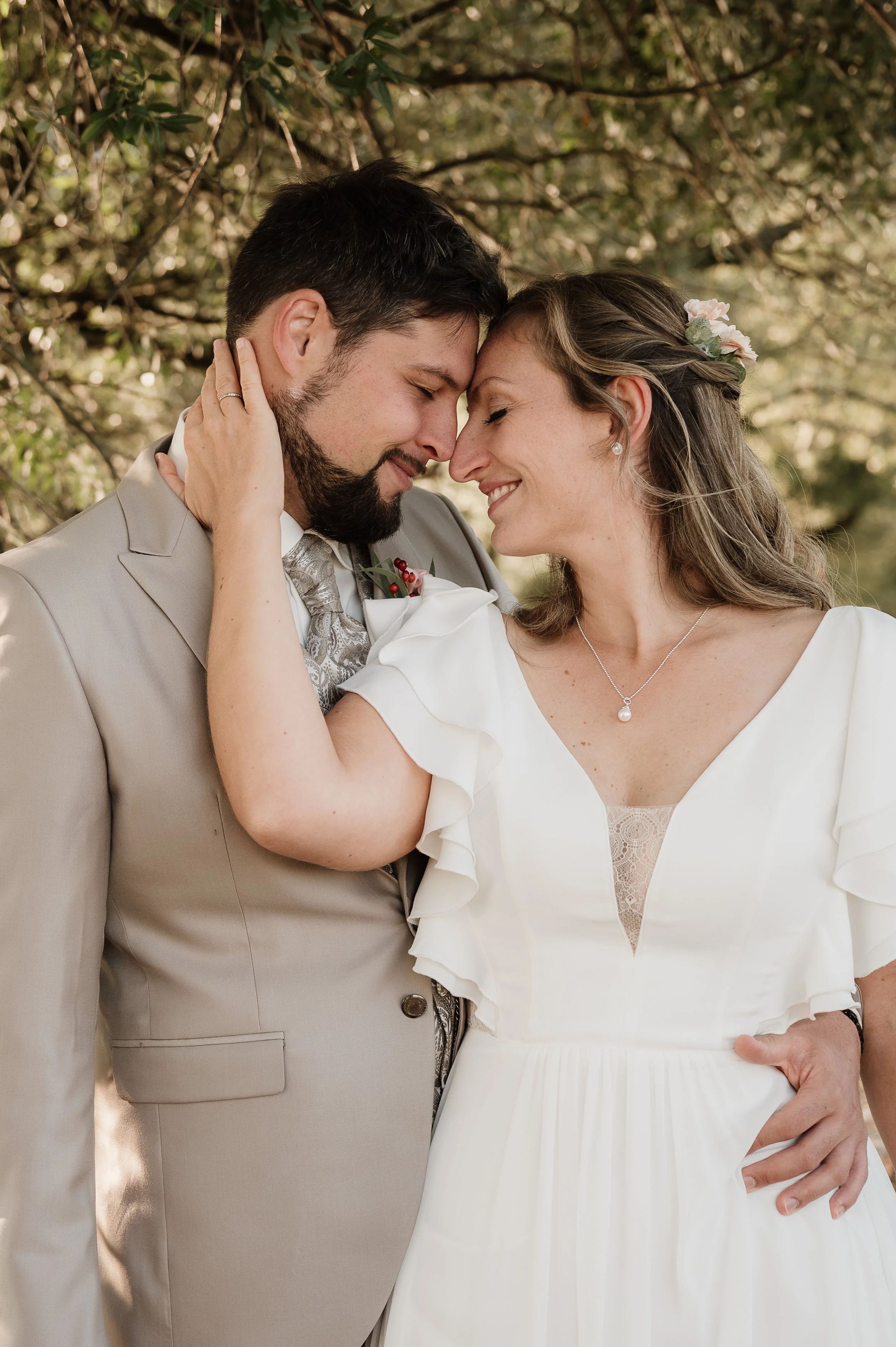 Ein Brautpaar steht sich mit ihren Stirn aneinander, umarmt und lächelt glücklich bei ihrer Hochzeit im Freien.