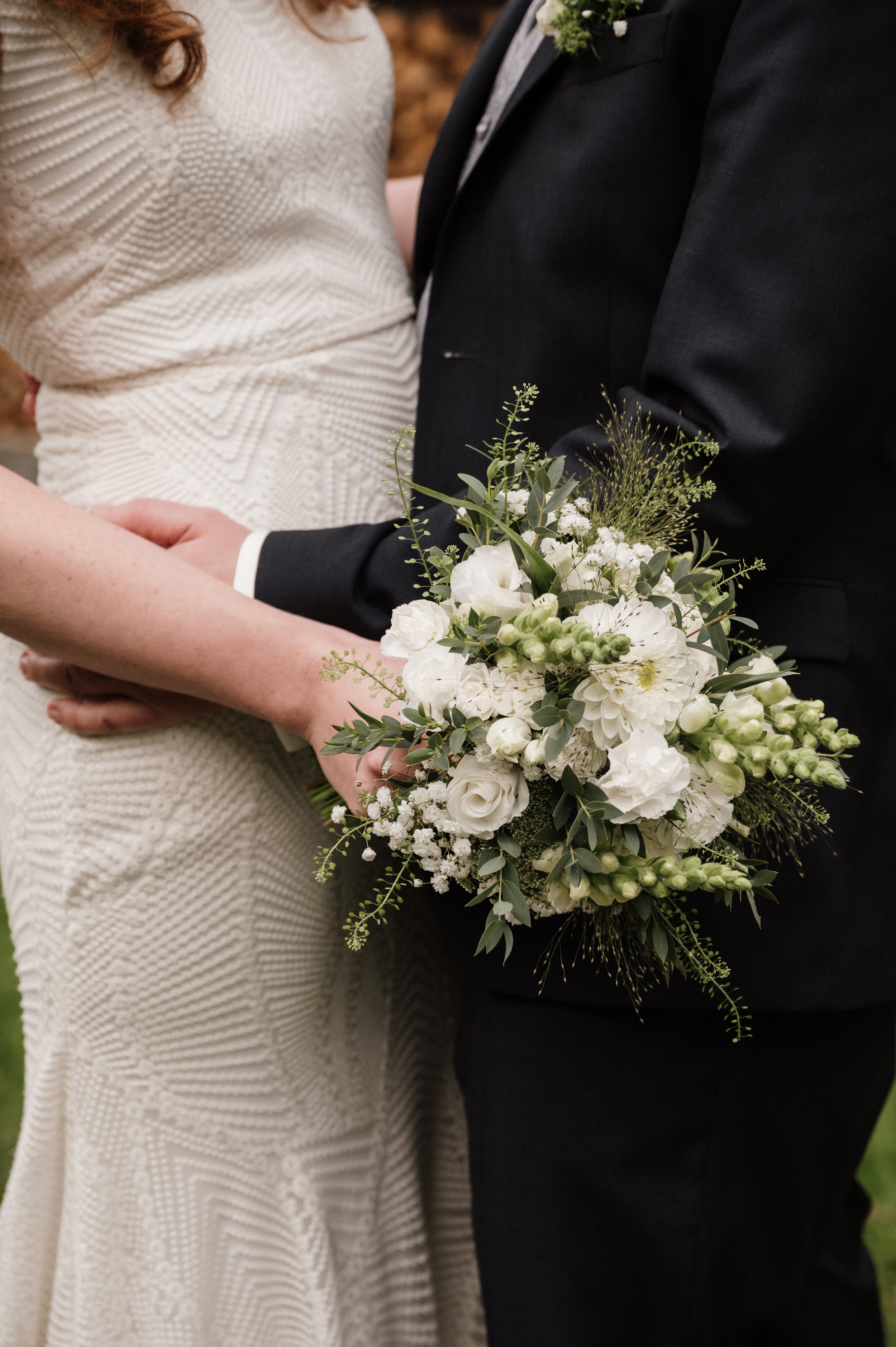 Braut und Bräutigam bei einer Hochzeitszeremonie, der Bräutigam hält einen Strauß weißen Blumen.