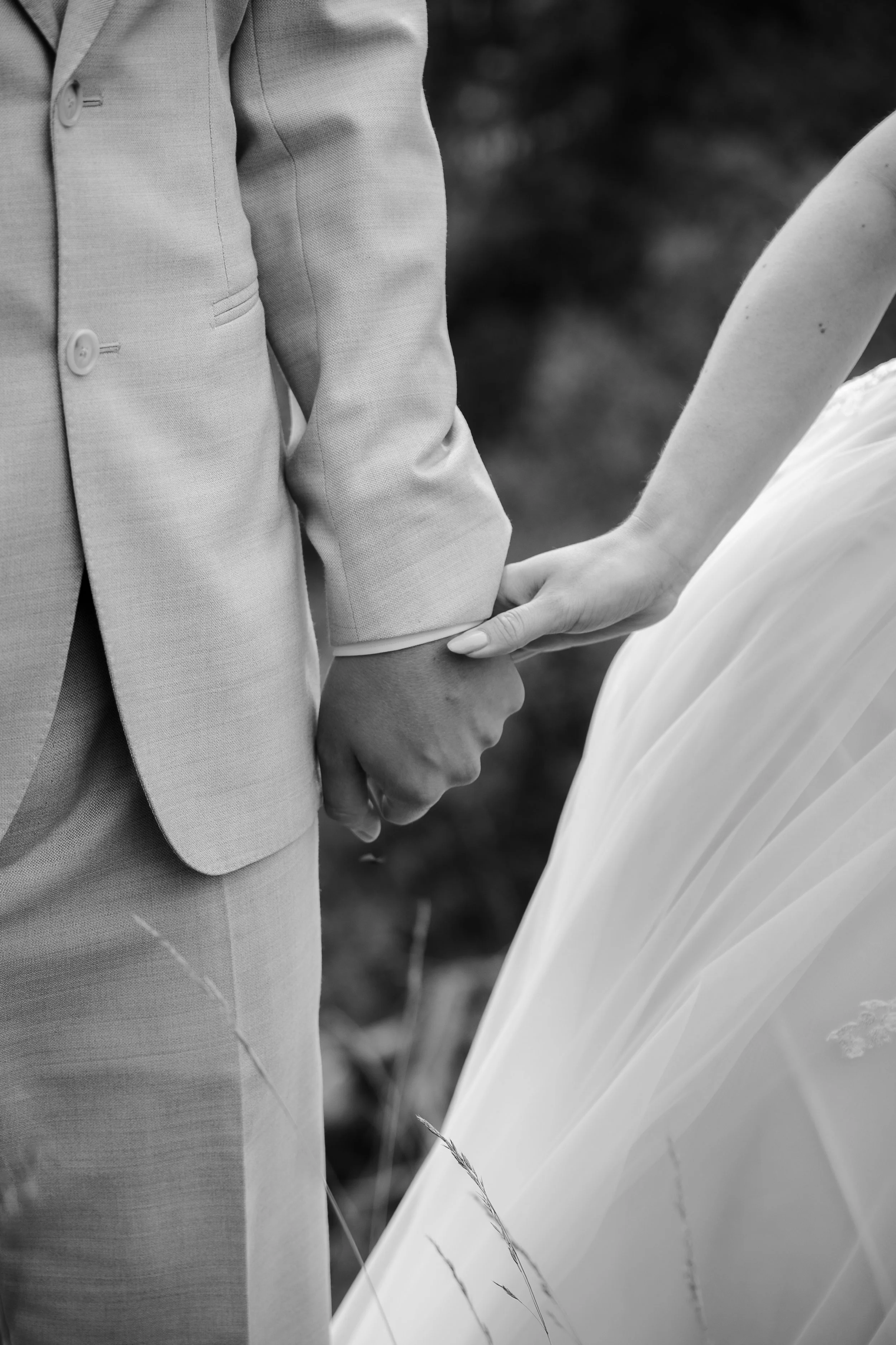 Nahaufnahme eines Paares, das sich bei einer Hochzeitszeremonie die Hände hält. Die Frau trägt ein weißes Brautkleid, der Mann einen hellen Anzug.