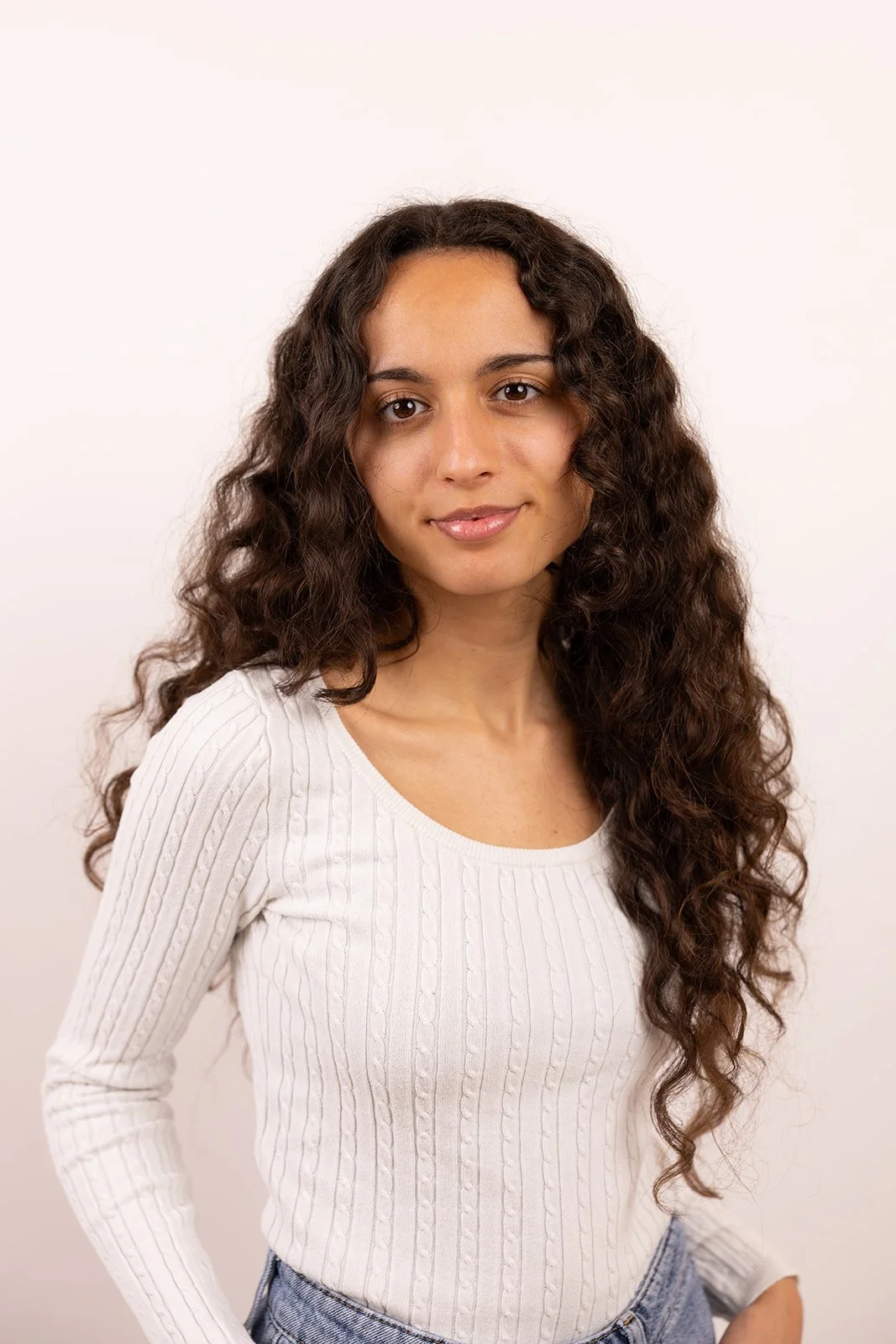 Porträt einer jungen Frau mit langen, lockigen braunen Haaren vor weißem Hintergrund.