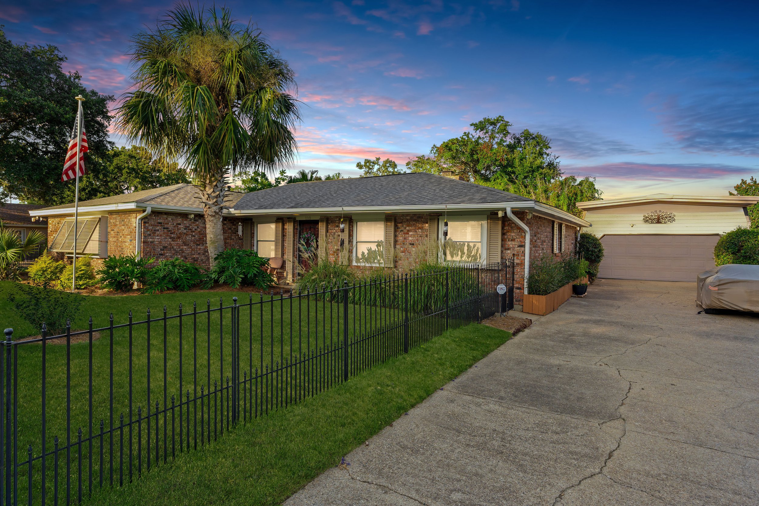 Single-story brick house with a front lawn, tall palm tree, and driveway at sunset.