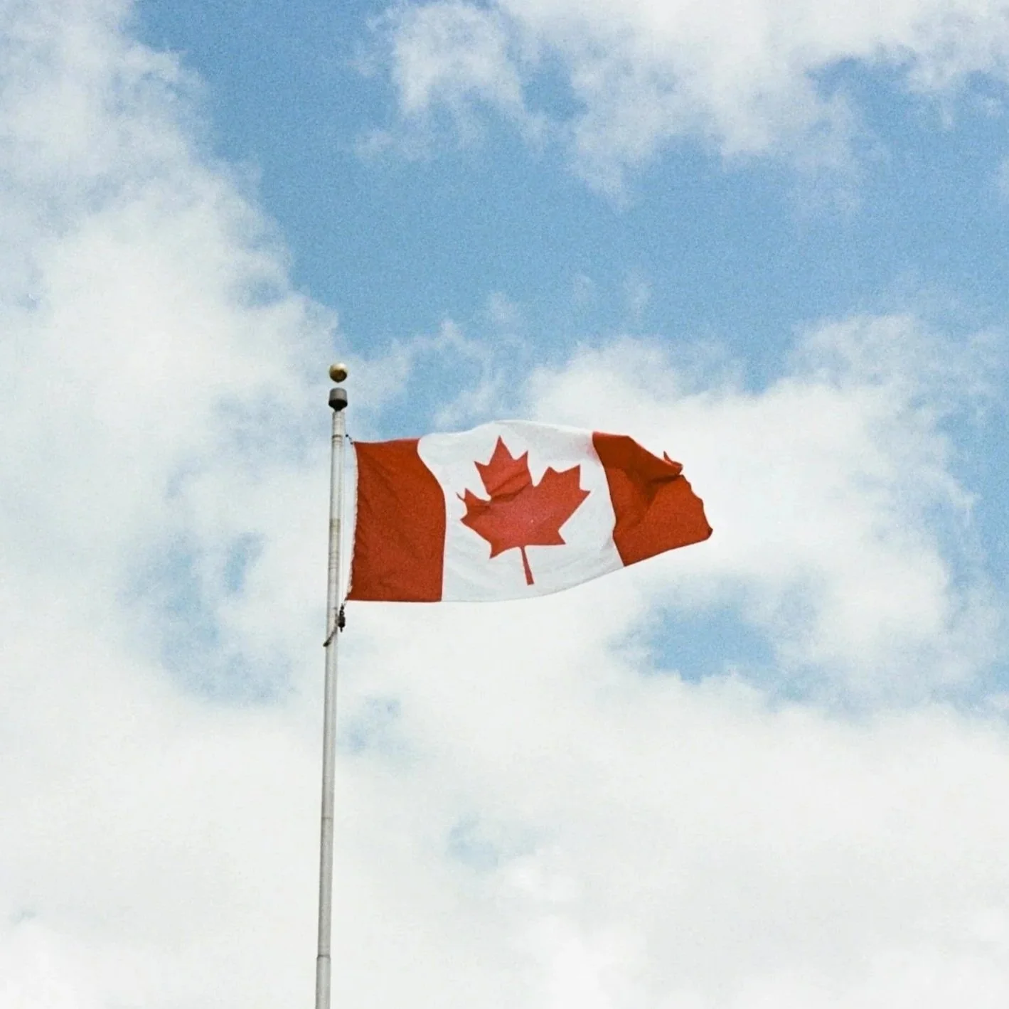 Canadian flag flying against a partly cloudy sky.