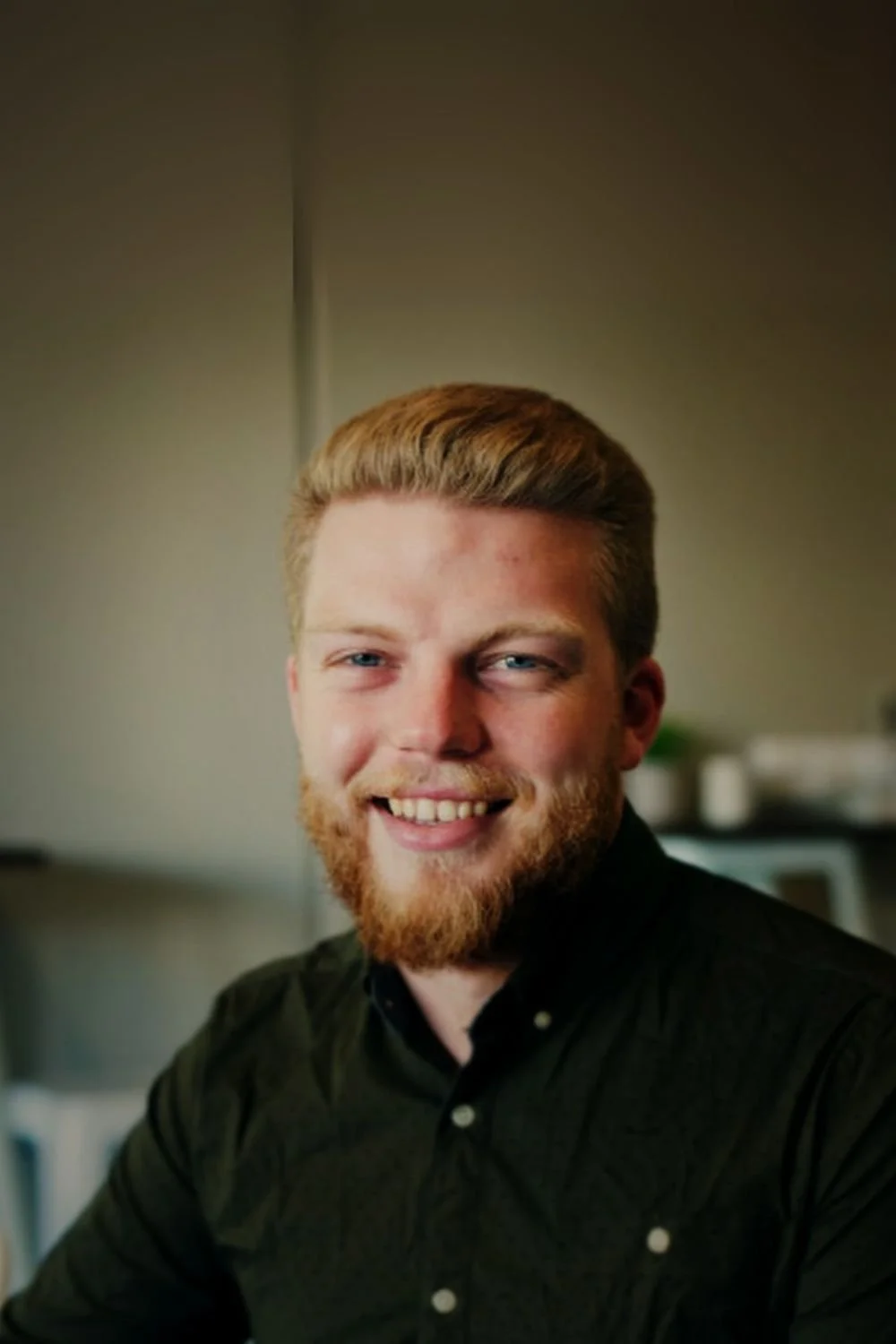 Young man with red hair and beard smiling in an indoor setting.