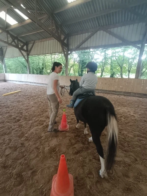 Un enfant en portage à cheval, lors d'une séance de médiation équine, effectuant un parcours moteur avec des cônes de signalisation.