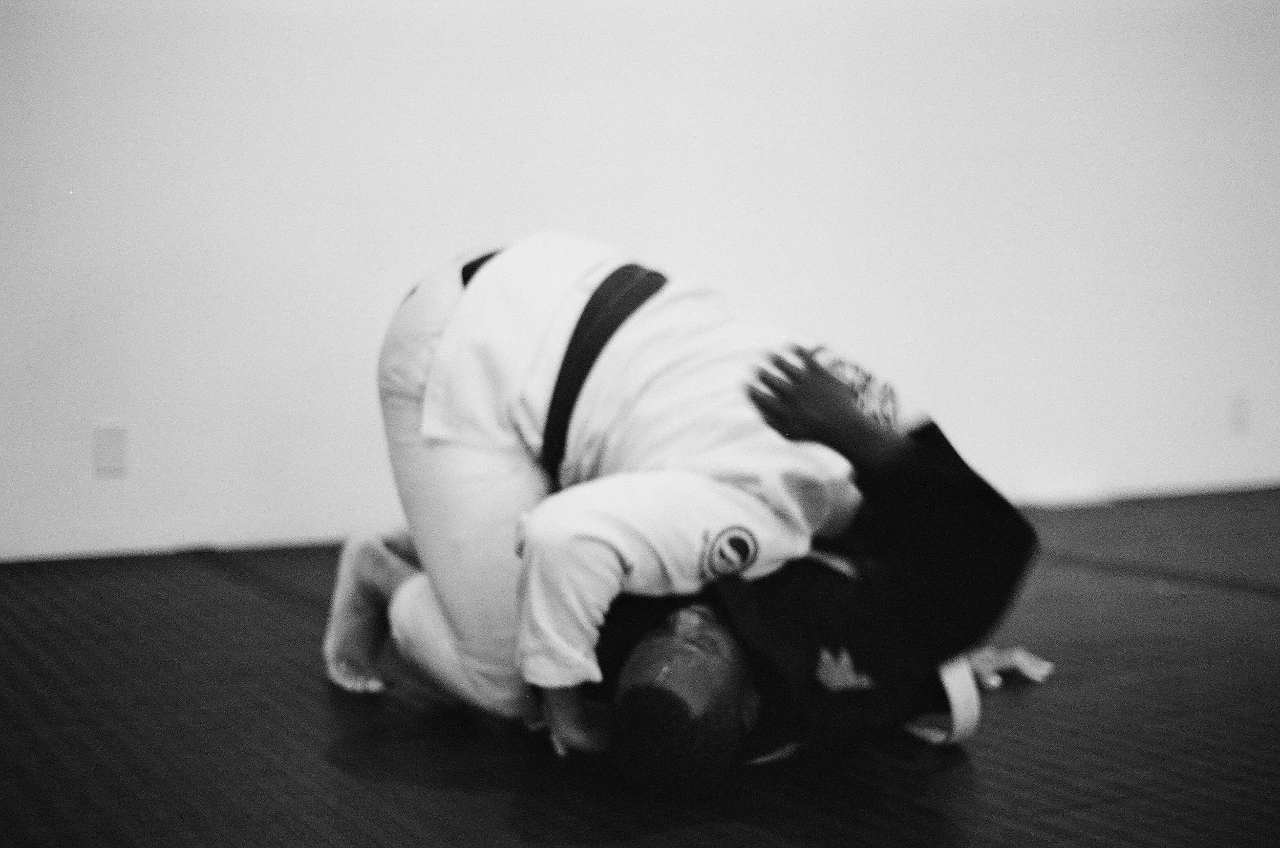 Two Brazilian Jiu-Jitsu practitioners in gis sparring on a mat, with one executing a submission move.