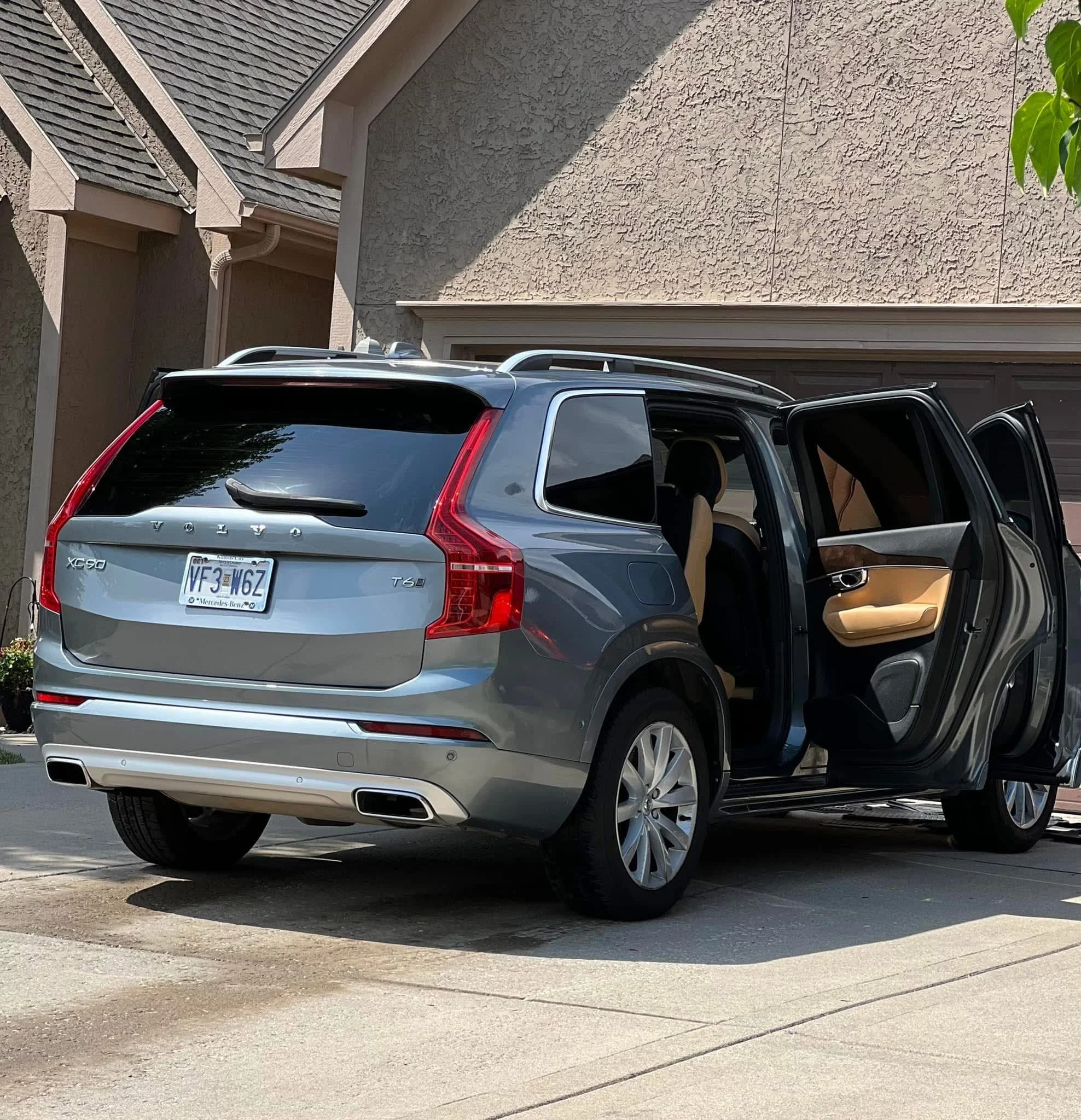 Gray Volvo XC90 SUV parked in front of a house with its rear and side doors open, showing tan interior seats.