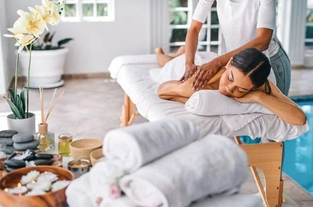 Woman receiving a massage in a bright, cozy spa room with towels, candles, and plants.