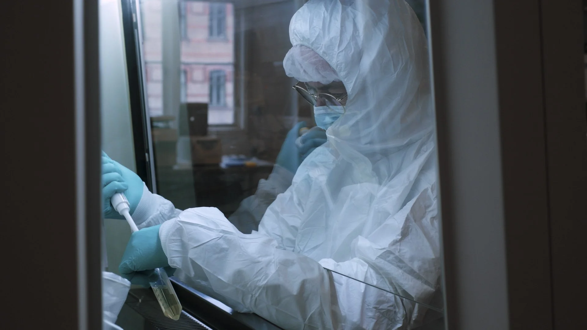 A scientist in full protective gear, including a hazmat suit, mask, and gloves, is working in a laboratory, handling a test tube.