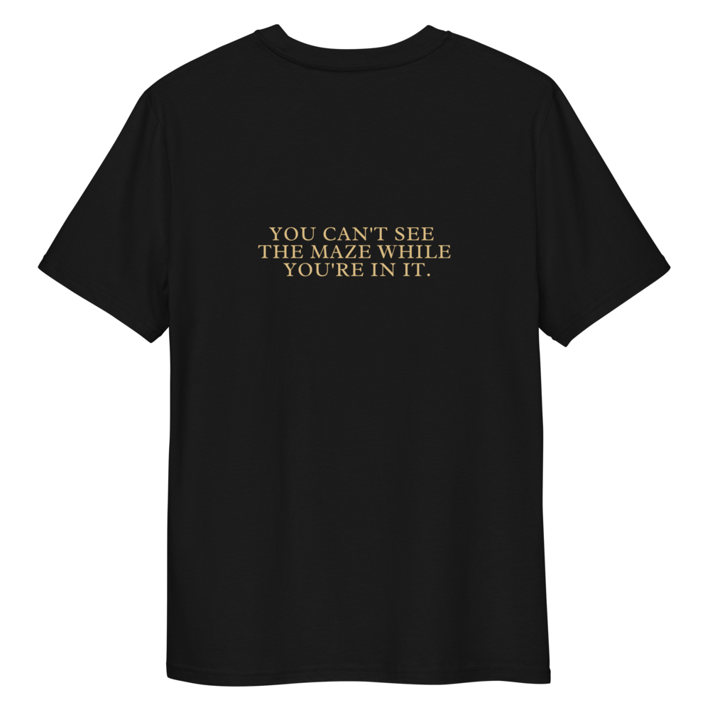 Back of a black T-shirt with the words “YOU CAN’T SEE THE MAZE WHILE YOU’RE IN IT.” in gold text.