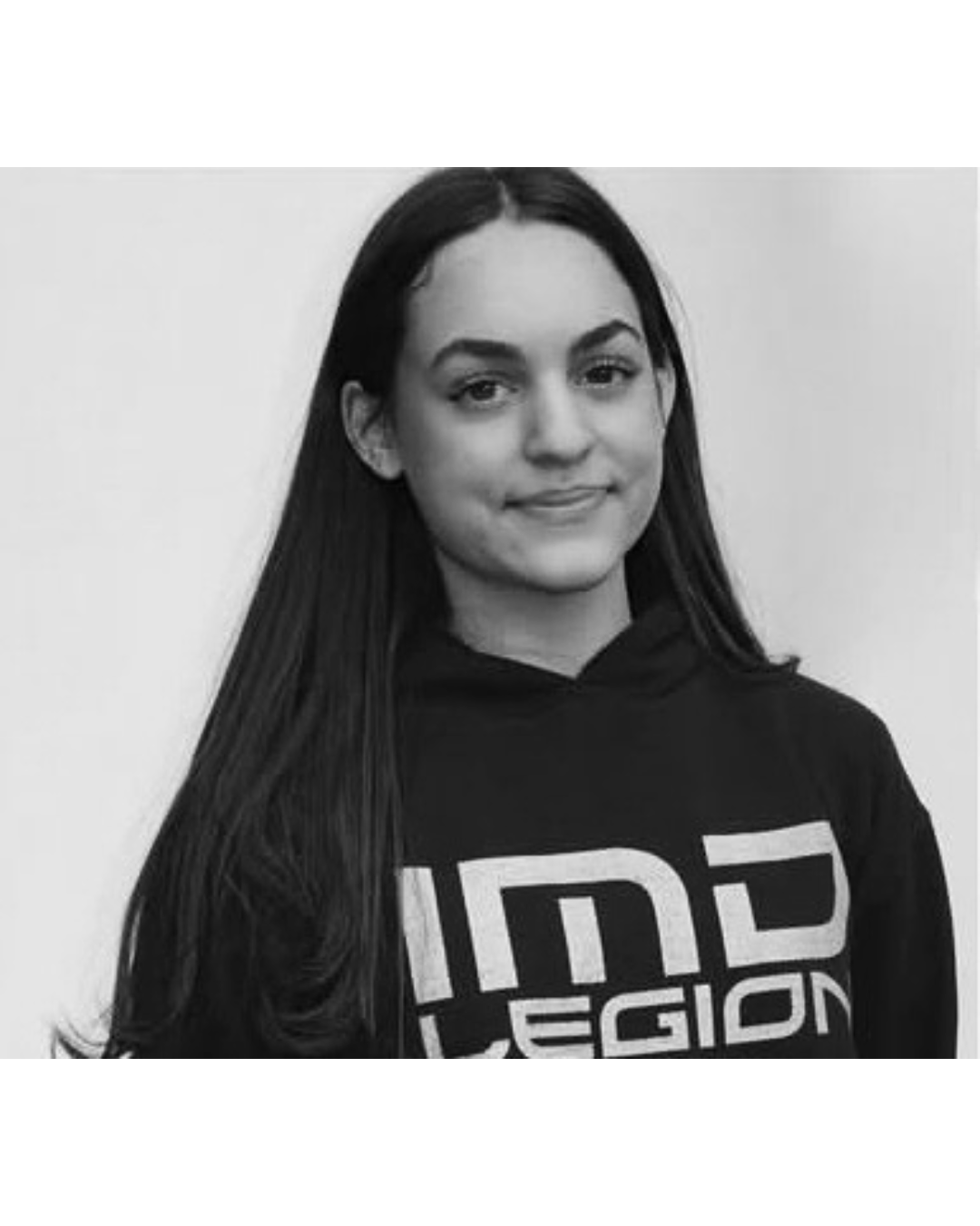 Young woman with long dark hair, wearing a black hoodie with 'IN3 LEGION' printed on it, looking at the camera with a slight smile, black and white photo.