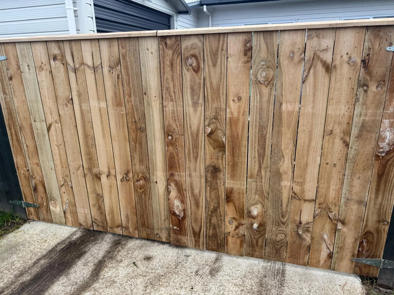 Wooden gate or fence made of vertical planks, installed outside, with metal hinges and latch, on a concrete surface.