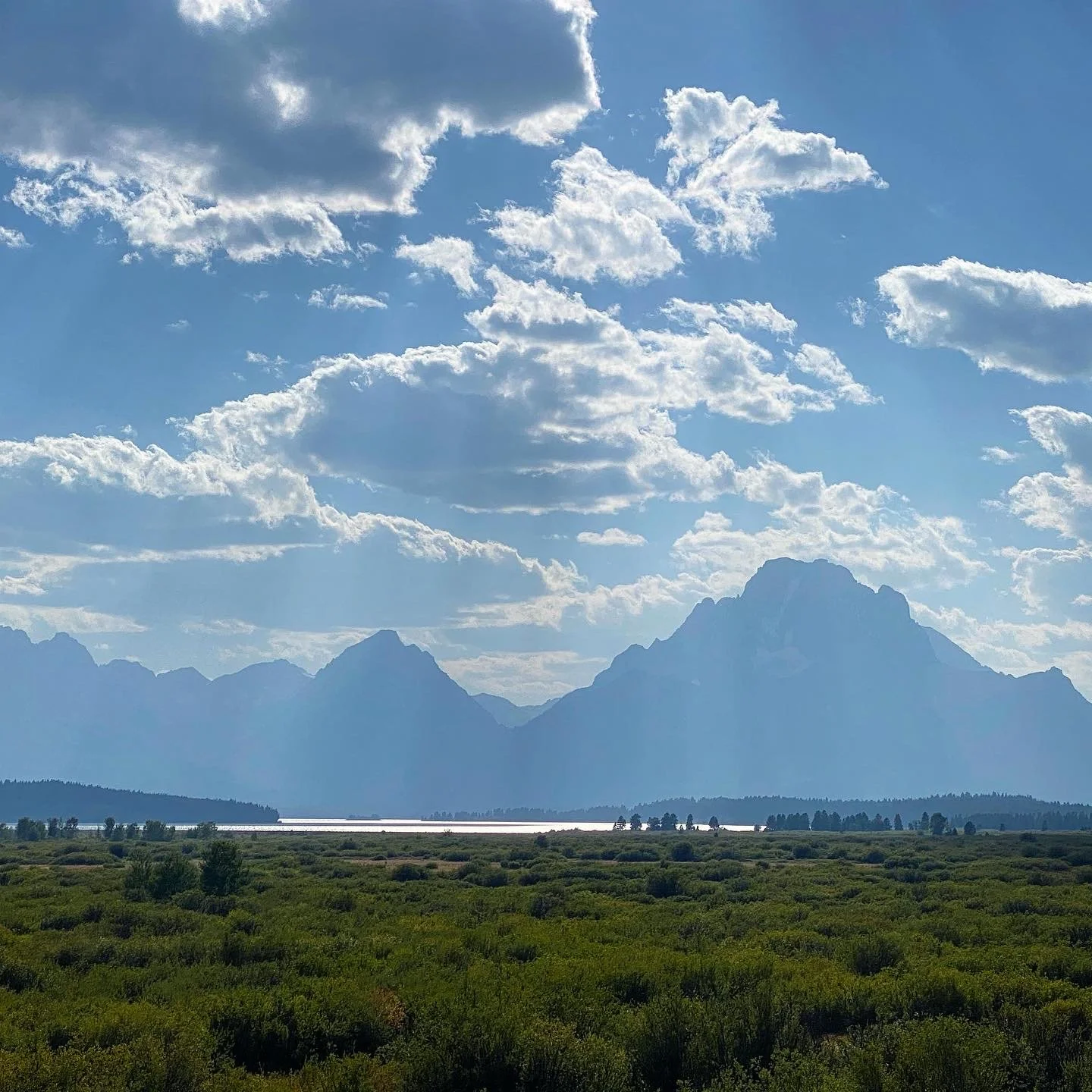 Landscape of distant mountains with cloud-filled sky and lush green vegetation in the foreground.