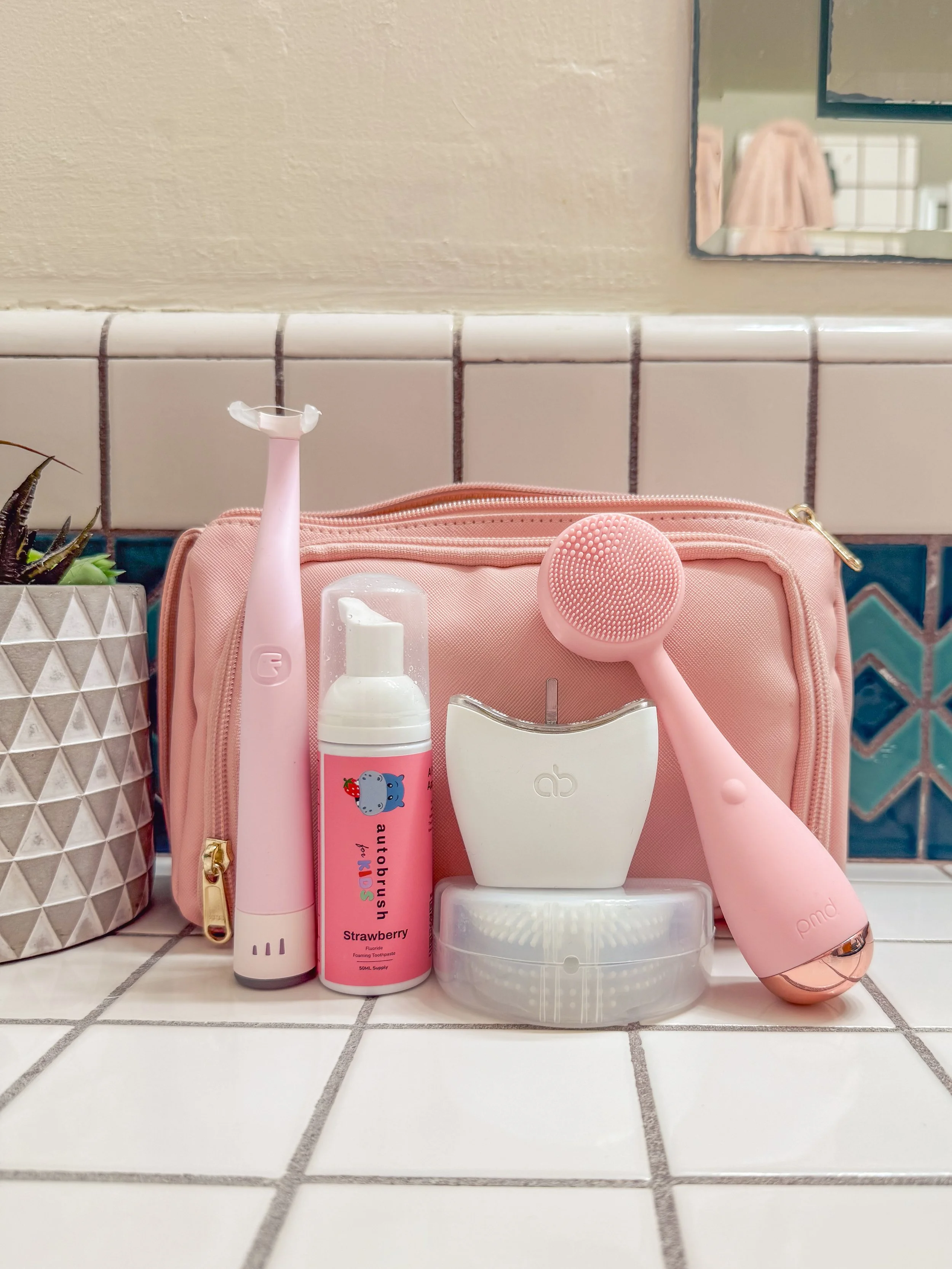 Flaus, Autobrush and PMD Clean in front of a pink toiletries bag