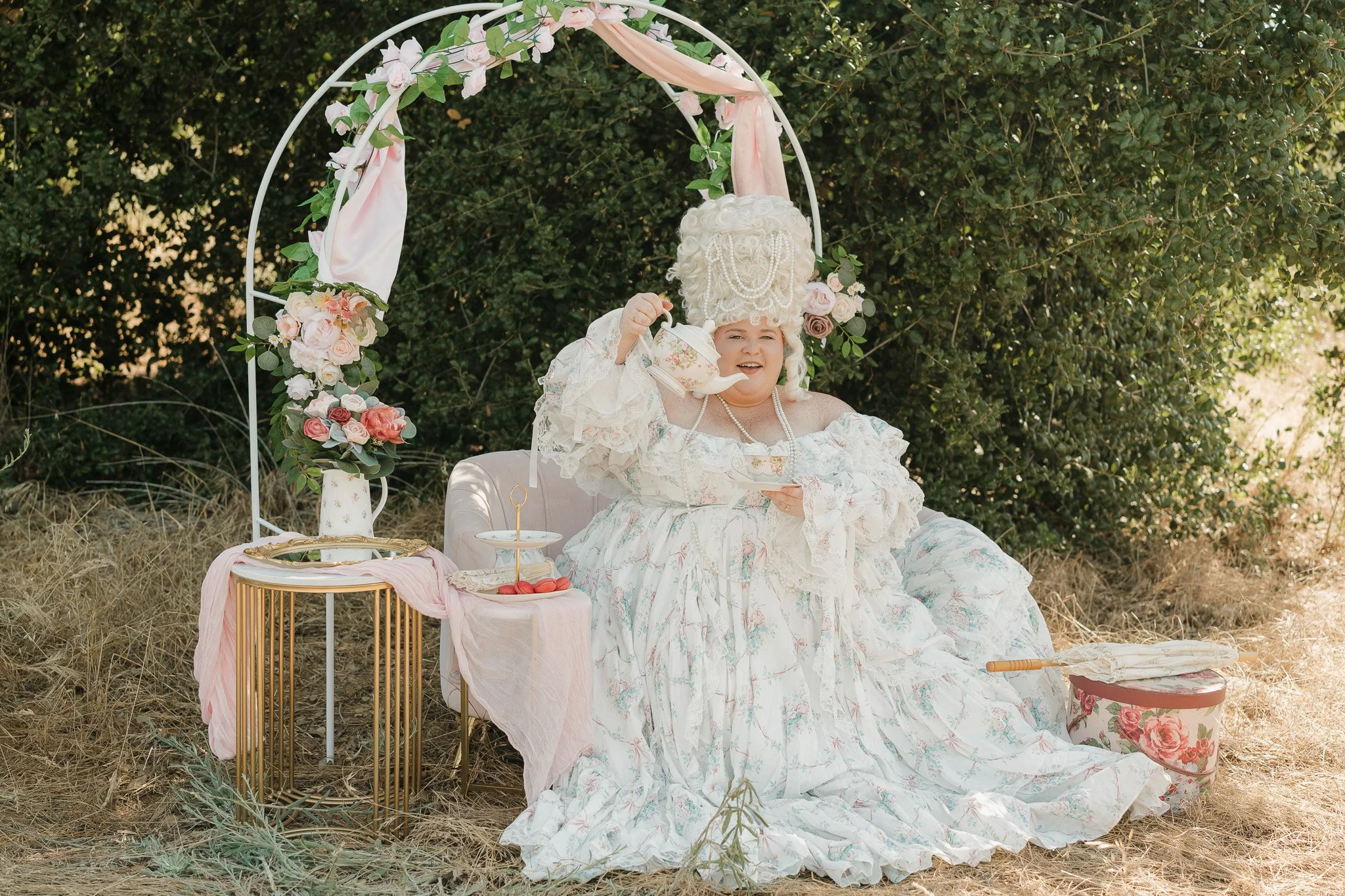 Woman sitting on a couch with an arch and tea party decor dressed in a plus size Selkie gown