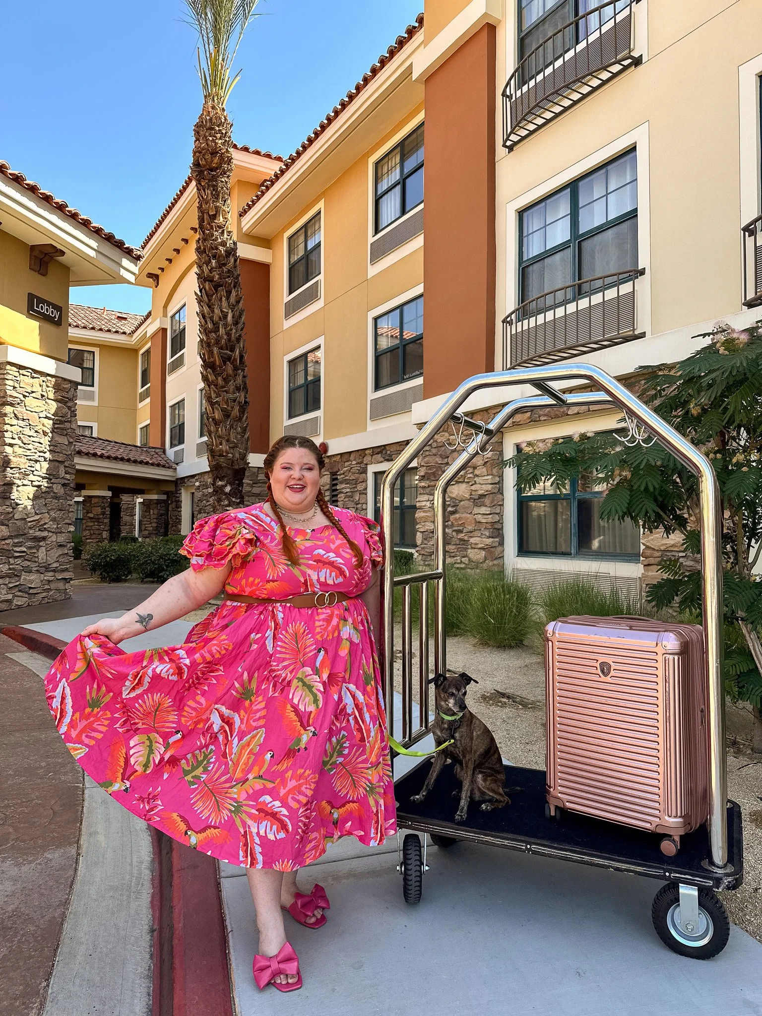 Plus size woman in front of a hotel with her luggage and dog.