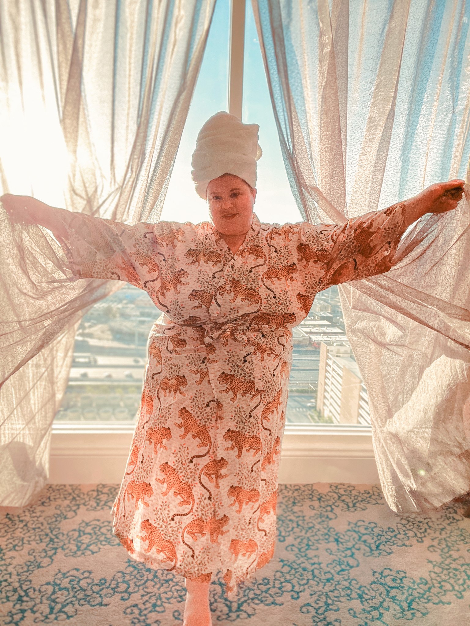 Plus size woman wearing a robe and towel on her head in a hotel room.