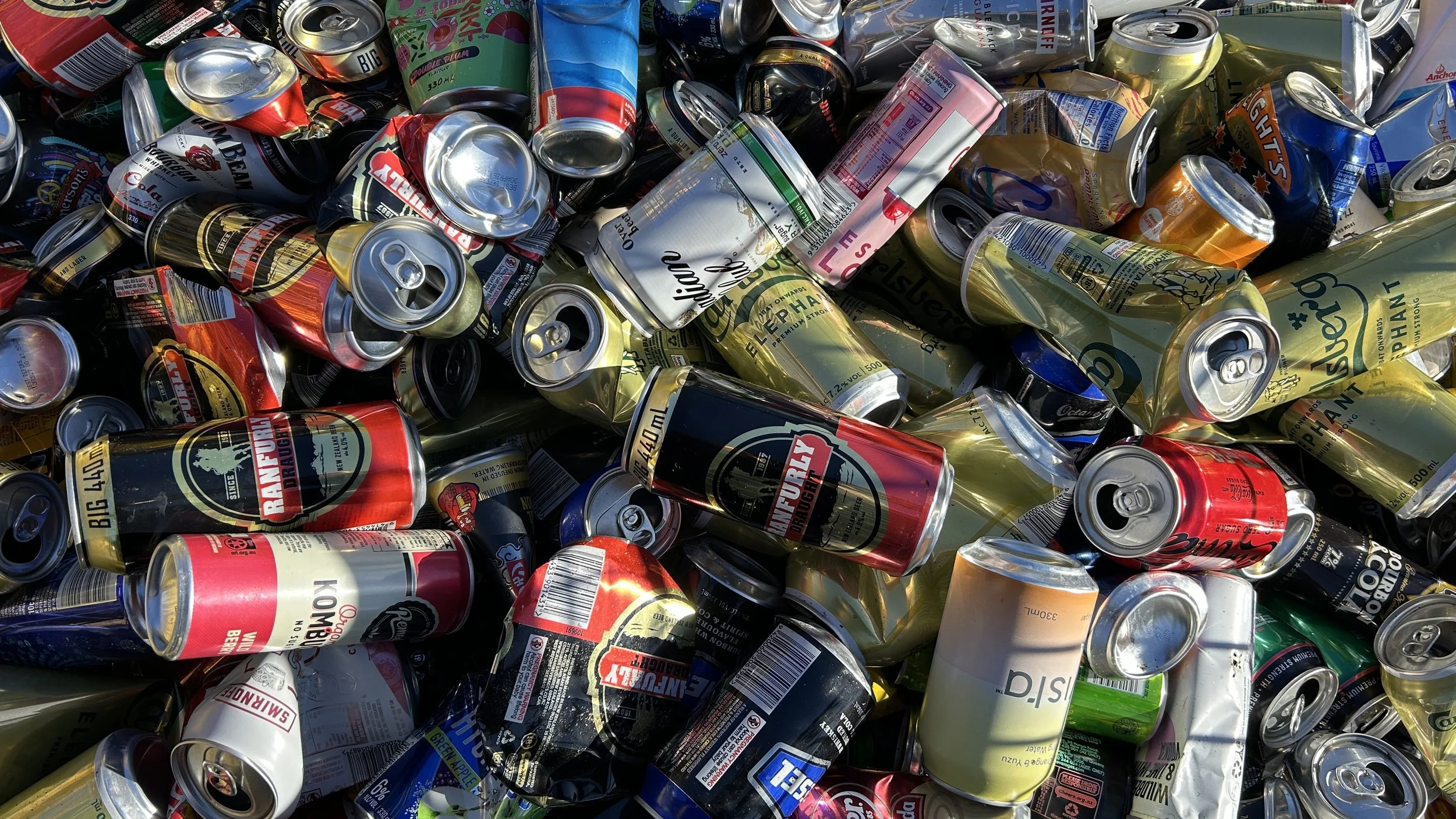 A large pile of crushed aluminum cans of various brands and colors, mostly red, yellow, black, and green.