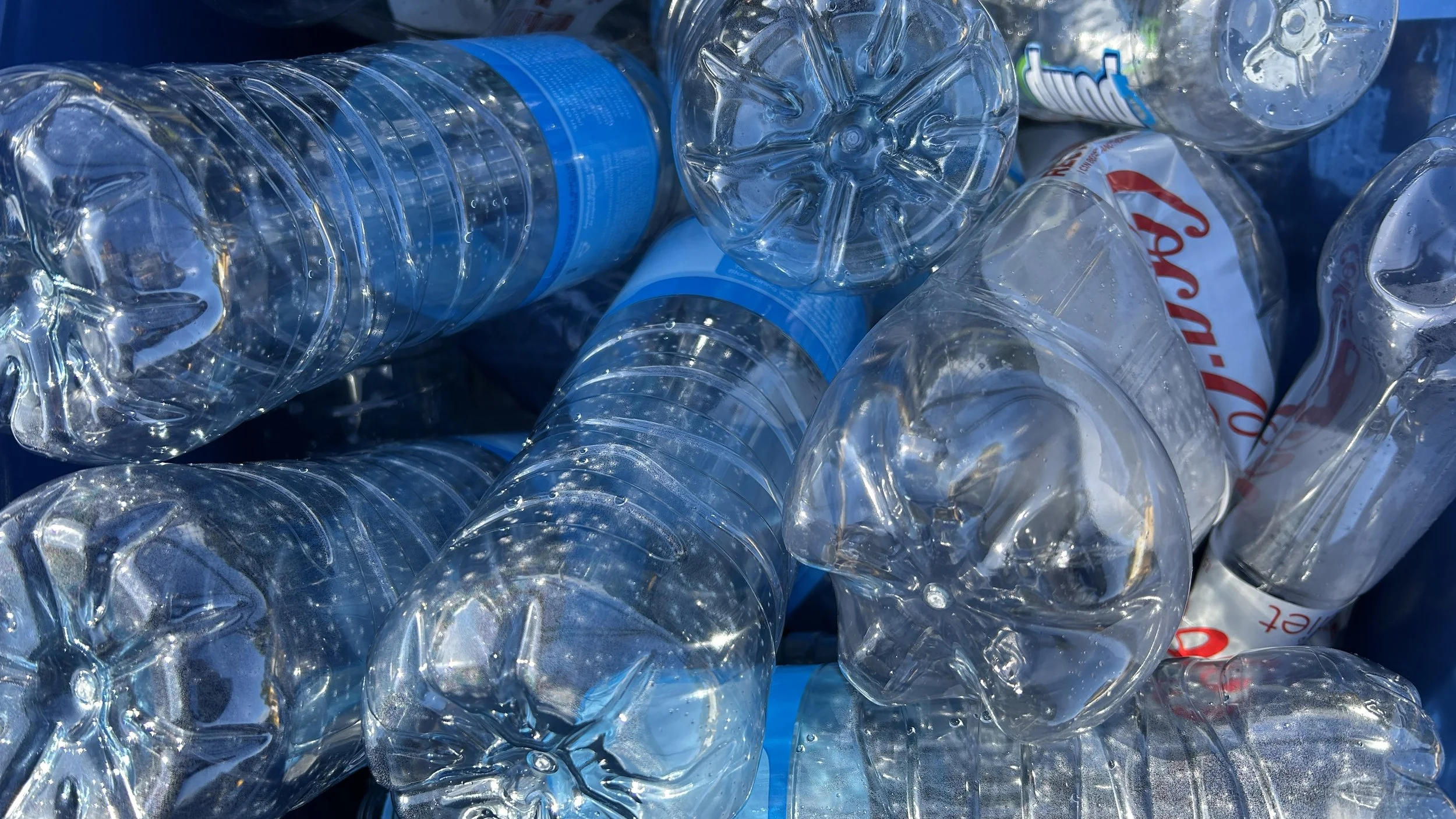 A pile of crumpled clear plastic water bottles with blue caps.
