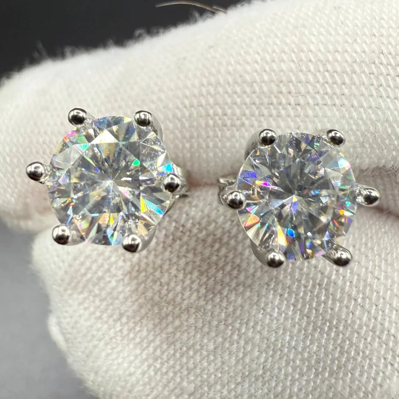 Pair of diamond stud earrings with round-cut stones set in silver prongs displayed on a white fabric background.
