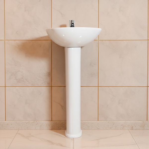 Lavabo de pedestal blanco en una pared de azulejos beige.