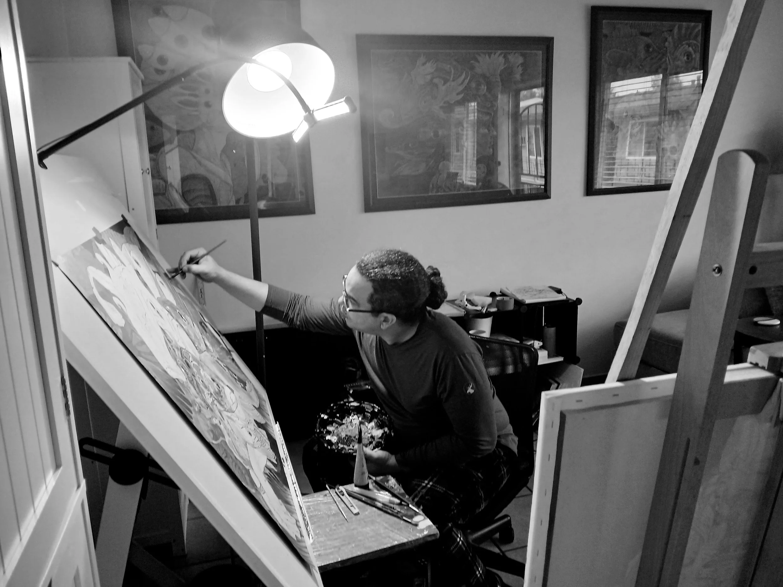 Artist Aurelio Milera painting on a large canvas in his studio, surrounded by framed artworks.