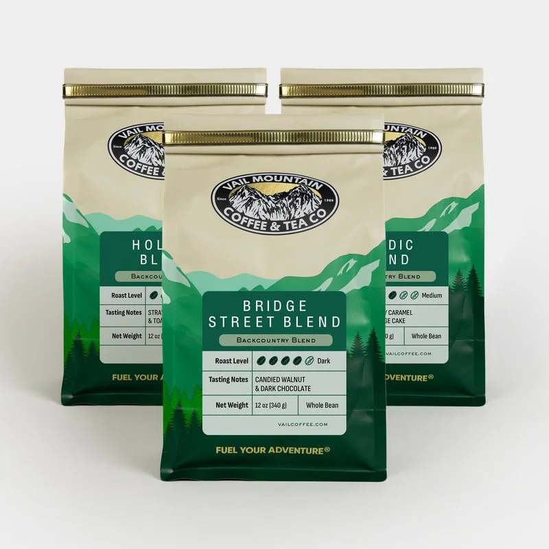 Three bags of Vail Mountain Coffee & Tea Co. coffee with green mountain landscape design on packaging.