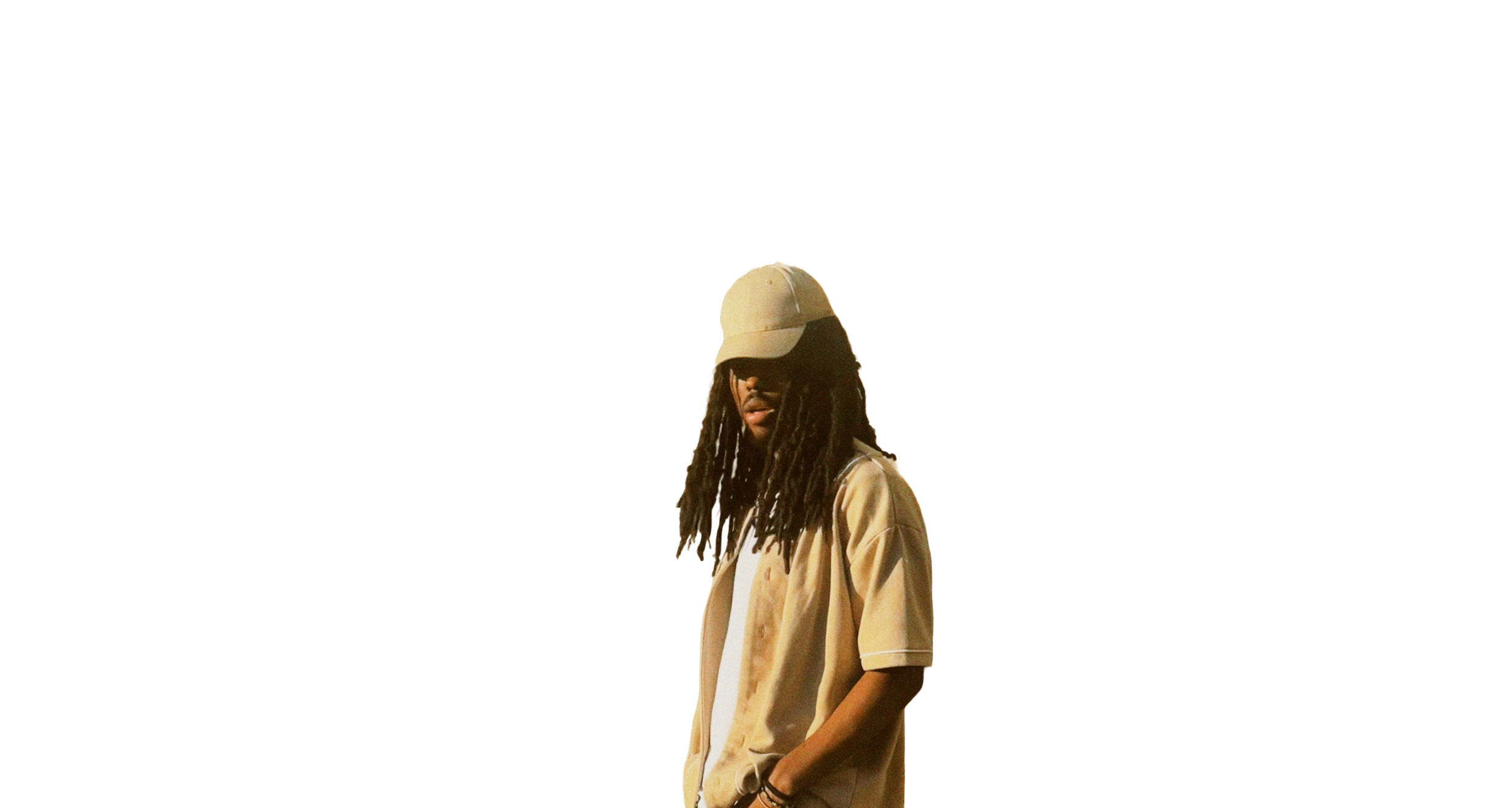 A person with long dreadlocks wearing a beige baseball cap and beige shirt stands against a white background.