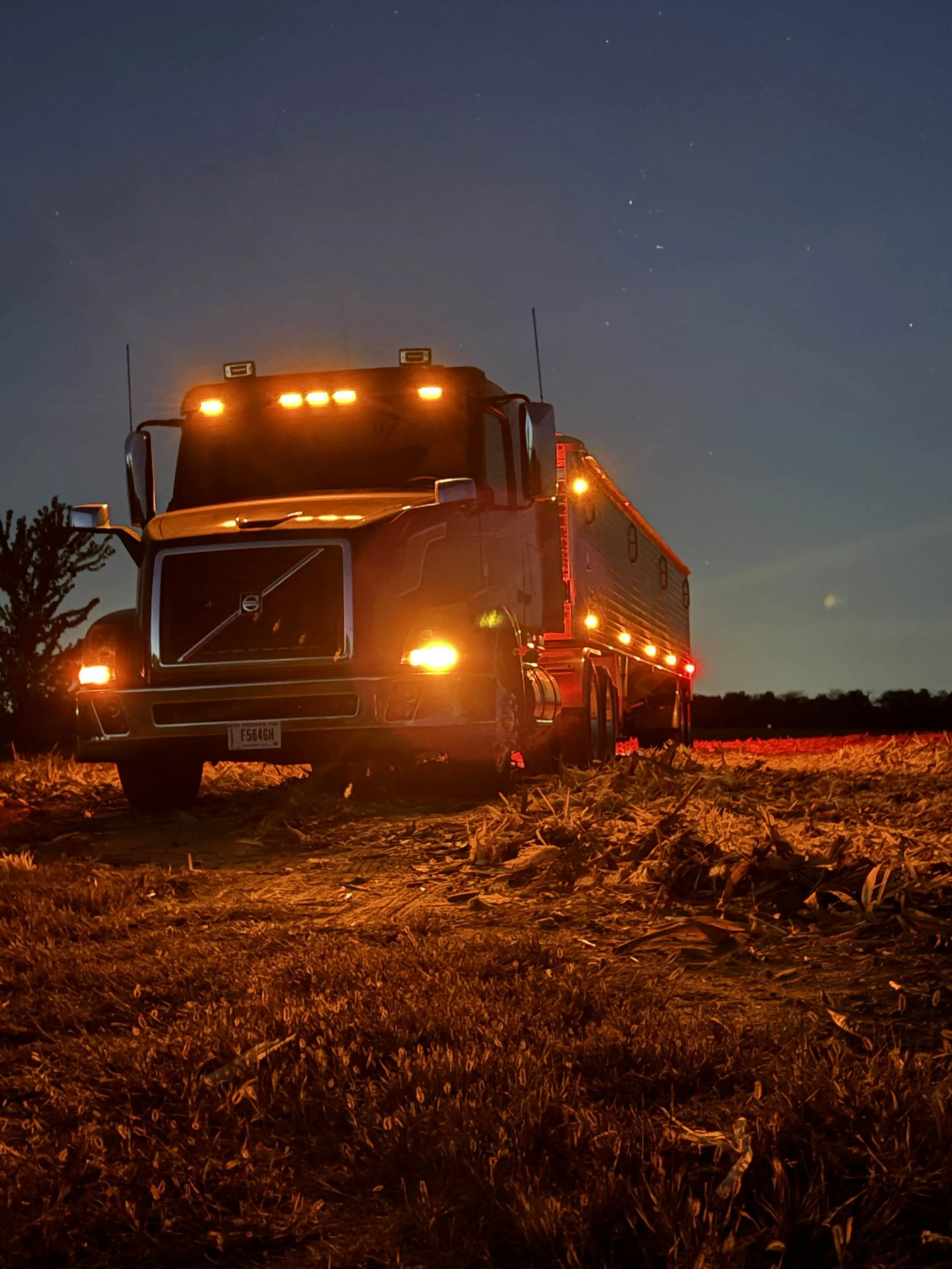 A large fire truck with bright lights on, parked on a dirt field at night under a starry sky.