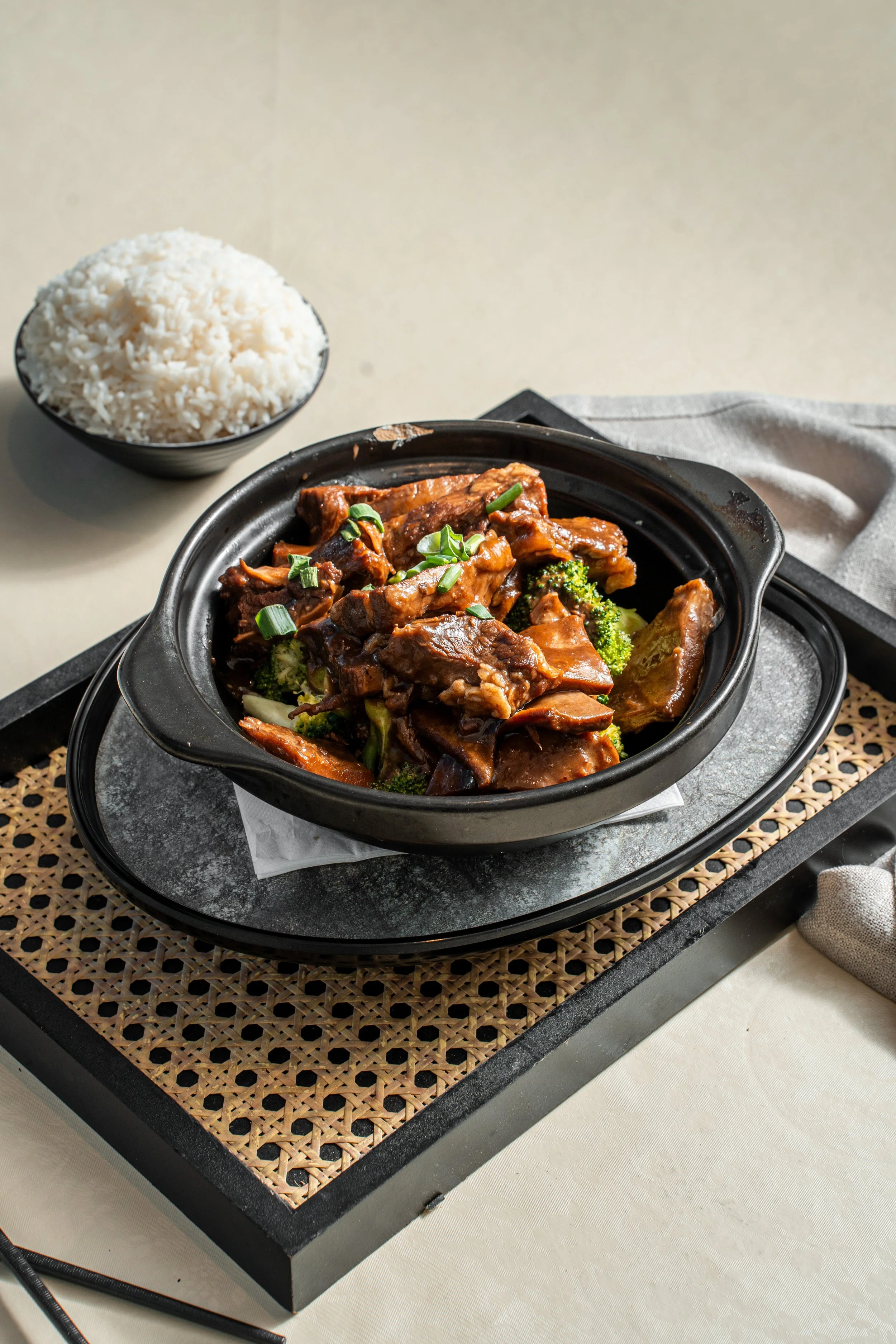A variety of Chinese dishes on a table, including dumplings in a bamboo steamer, bowls of white rice, fried chicken pieces with lettuce, stir-fried meat with vegetables, and a plate of meatballs with dipping sauce.