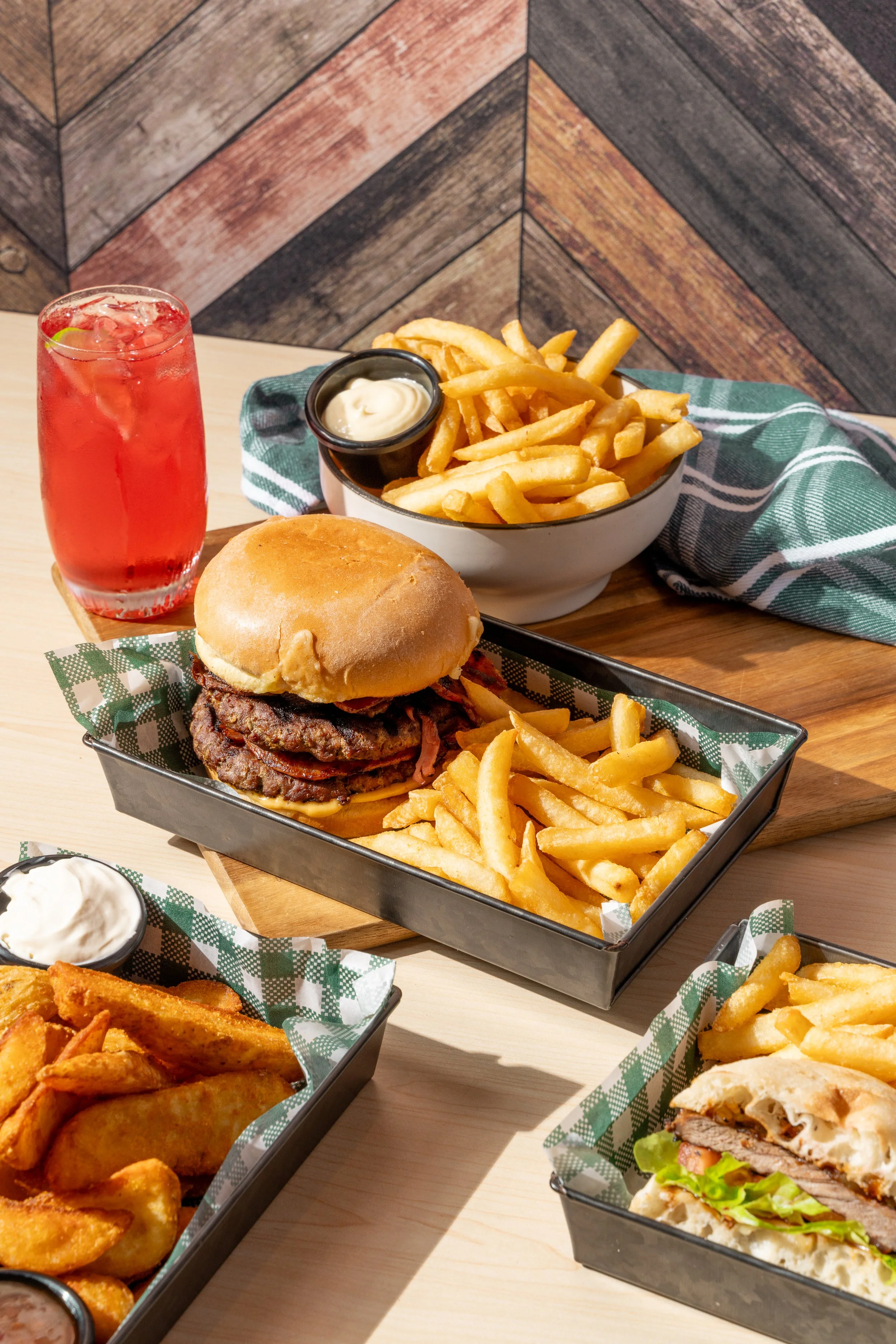 A meal with a burger, French fries, and a cold drink on a wooden table.