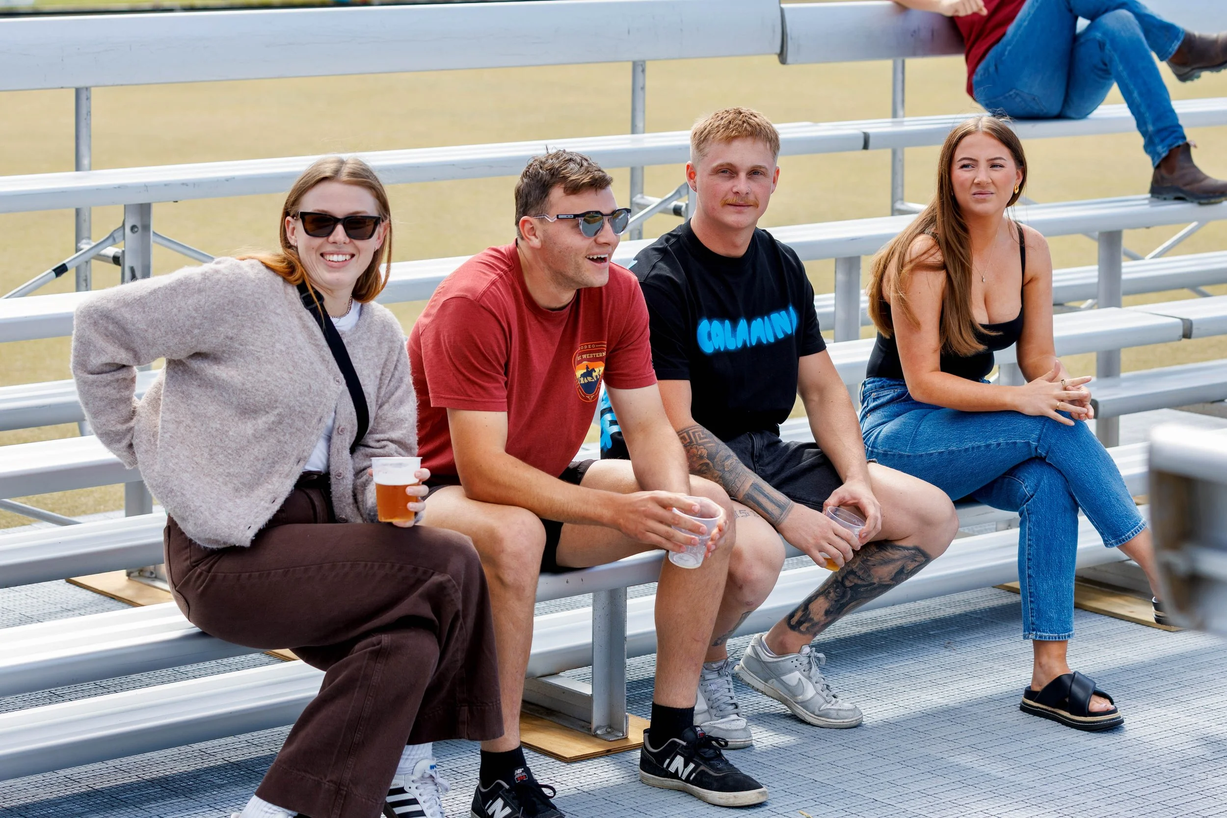 Four friends sitting on stadium bleachers, enjoying drinks and casual conversation outdoors.
