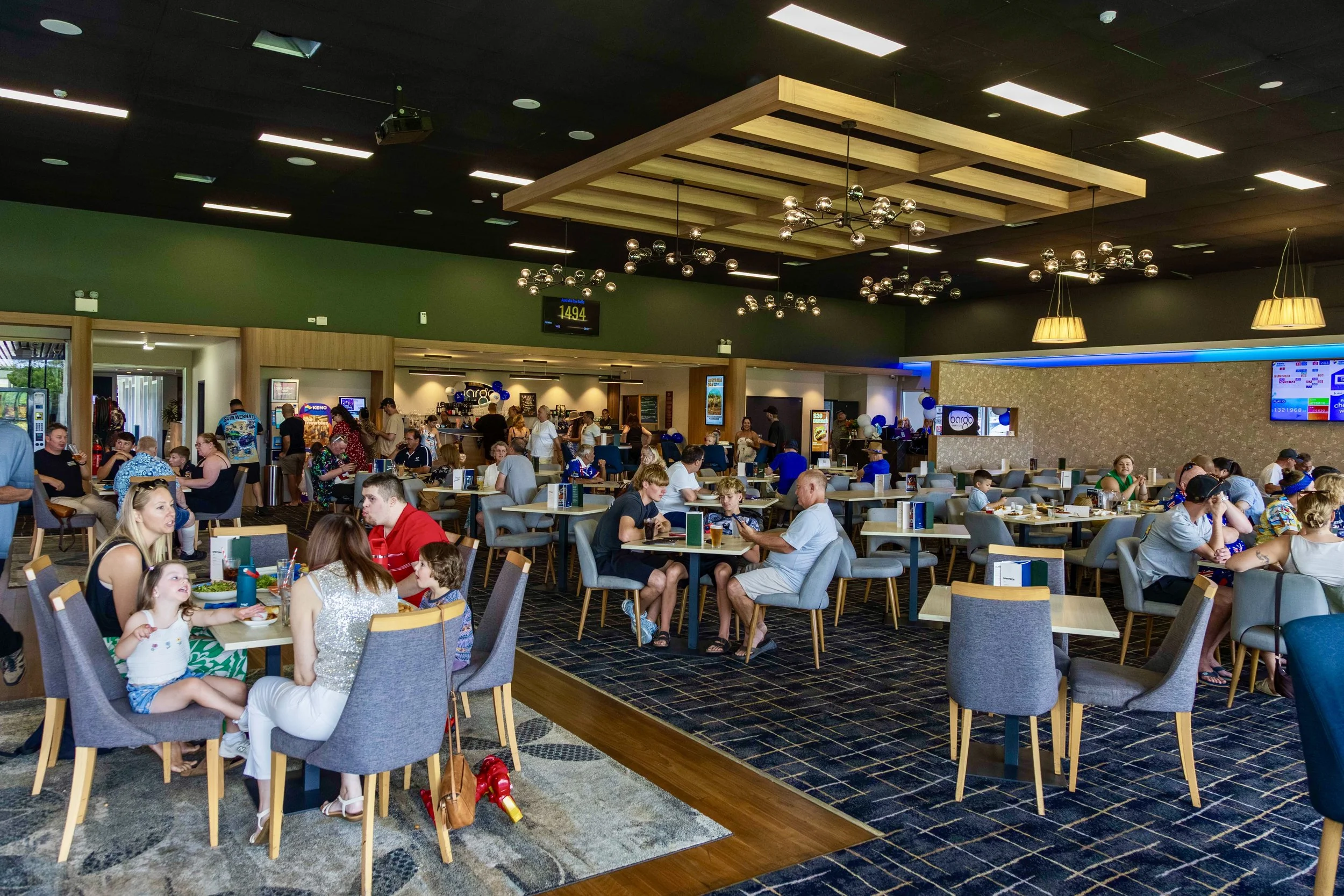 A busy indoor restaurant or cafe filled with people, children, and activities, with modern lighting and decor.