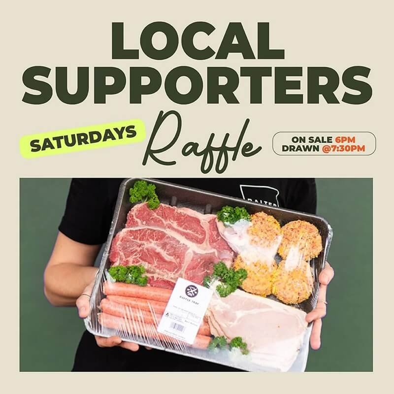 A person holding a tray of raw meat including marbled beef, chicken, and sausages, garnished with parsley.