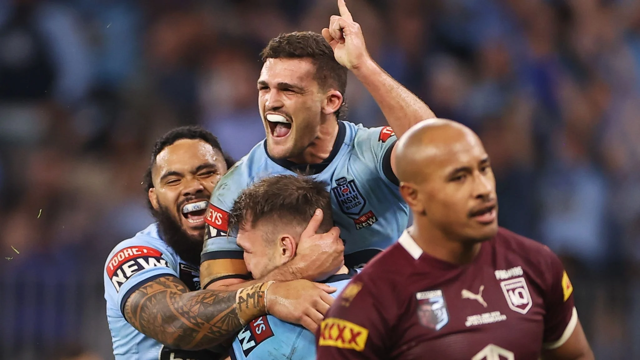 Rugby players celebrating on the field, with one jumping on others, showing excitement and joy.