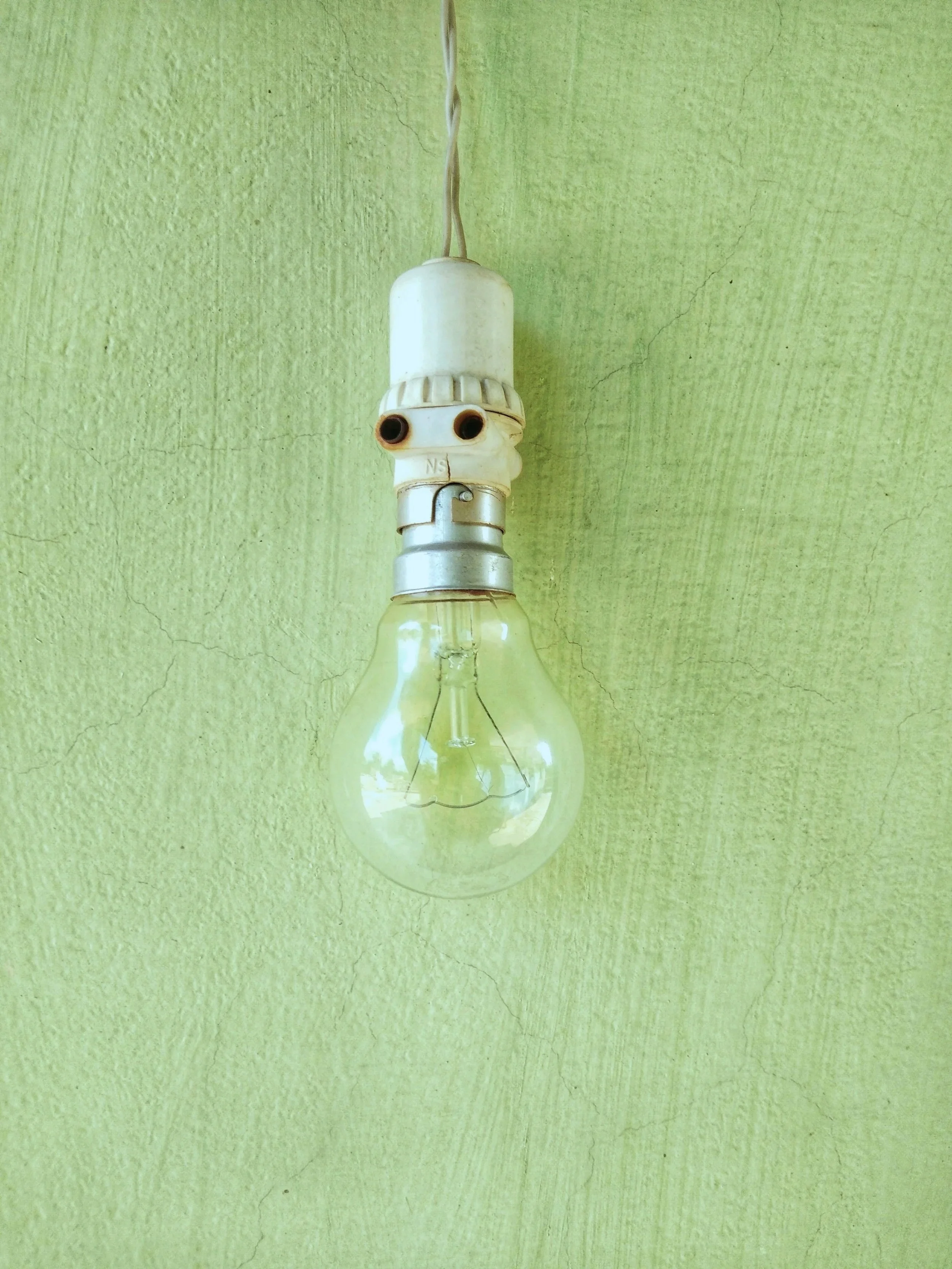 An exposed light bulb hanging from a ceiling on a green textured wall.