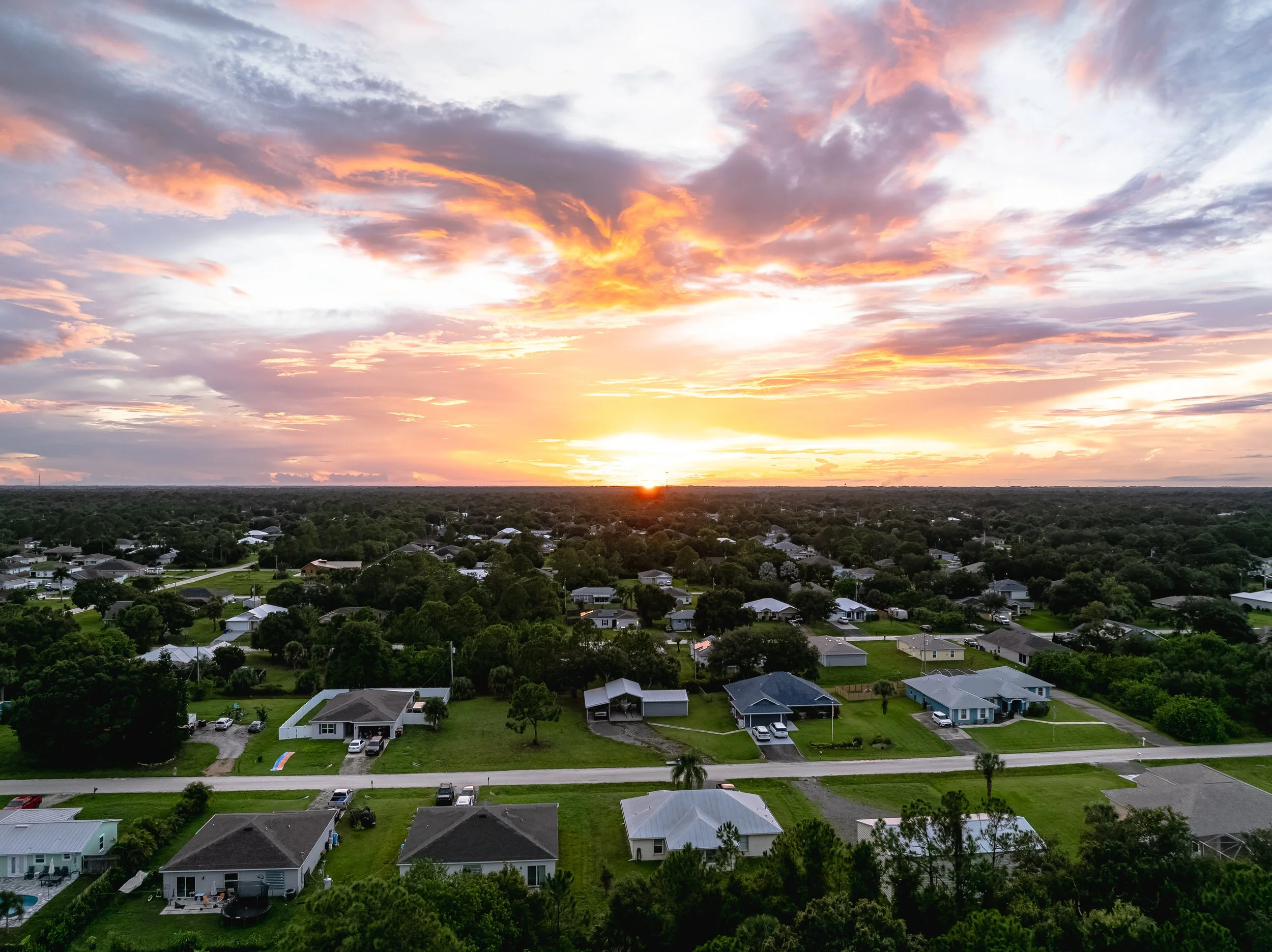 Sunset over a suburban neighborhood with houses, trees, and a colorful sky.