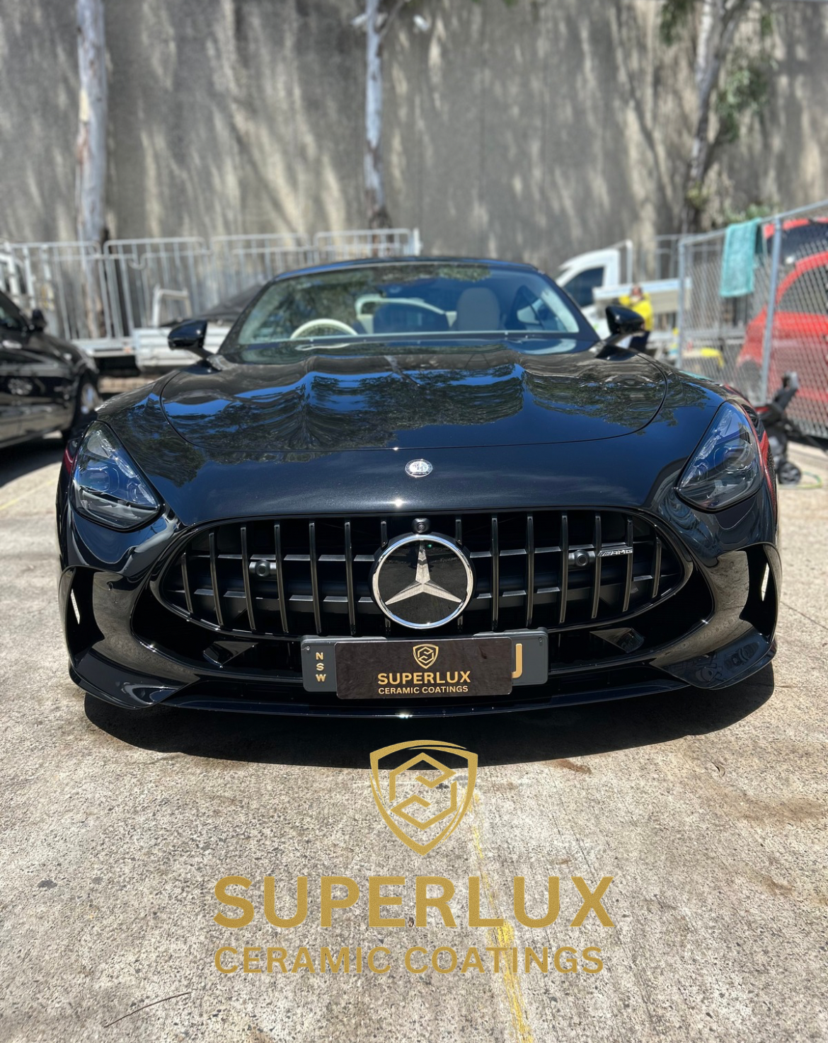 A black Mercedes-Benz sports car parked outdoors, with a large Mercedes emblem on the front grille, and a SUPERLUX CERAMIC COATINGS logo on the ground.