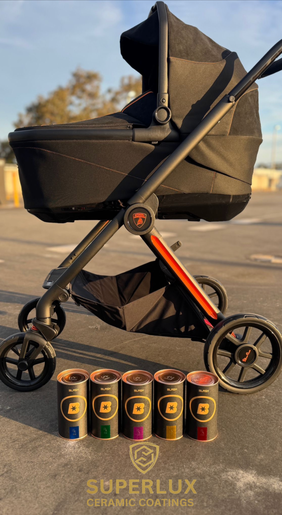 A black baby stroller with orange accents parked outdoors on a pavement at sunset, with five cans of Superlux ceramic coatings in front and a logo at the bottom reading "Superlux Ceramic Coatings."