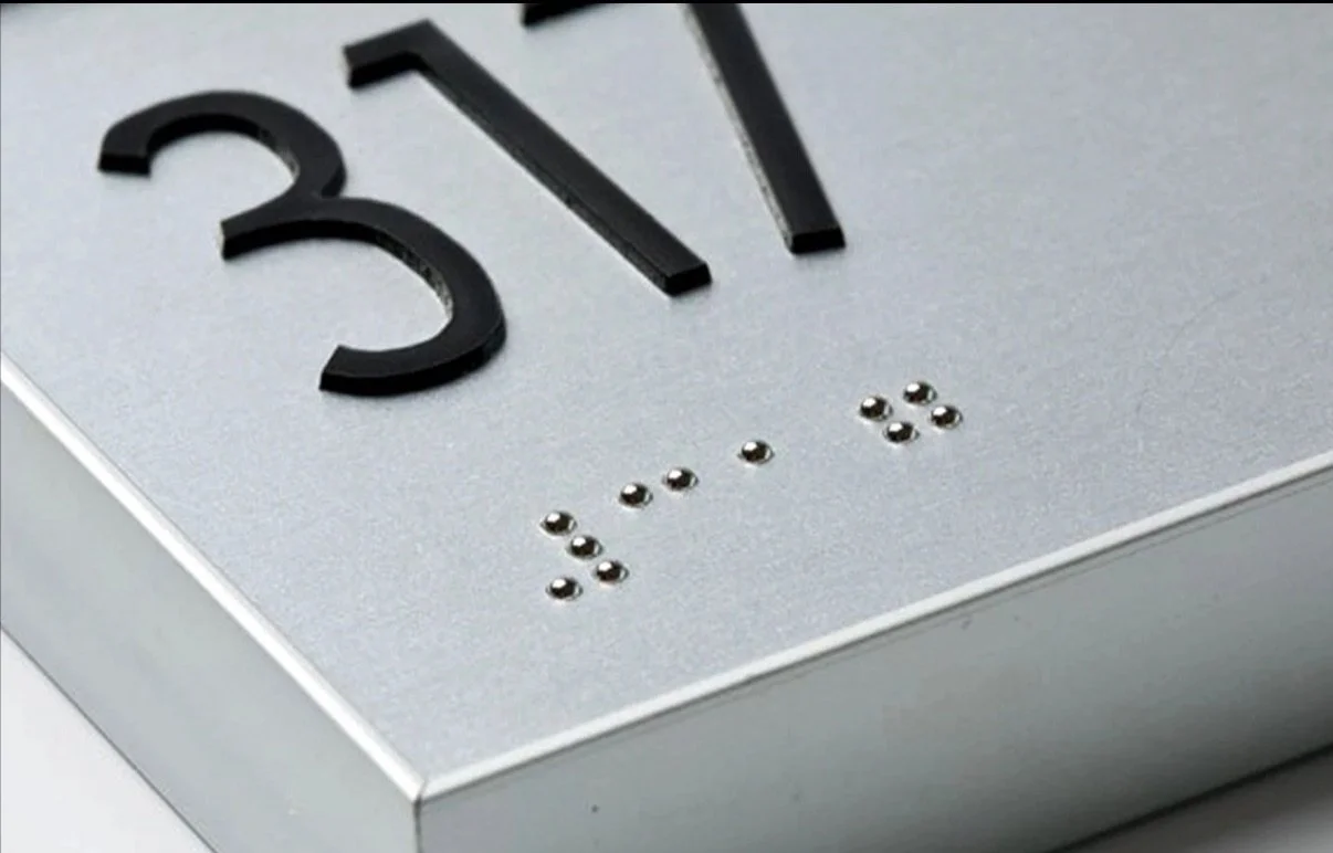 Close-up of a ADA sign with black raised numbers and braille dots indicating the room number.