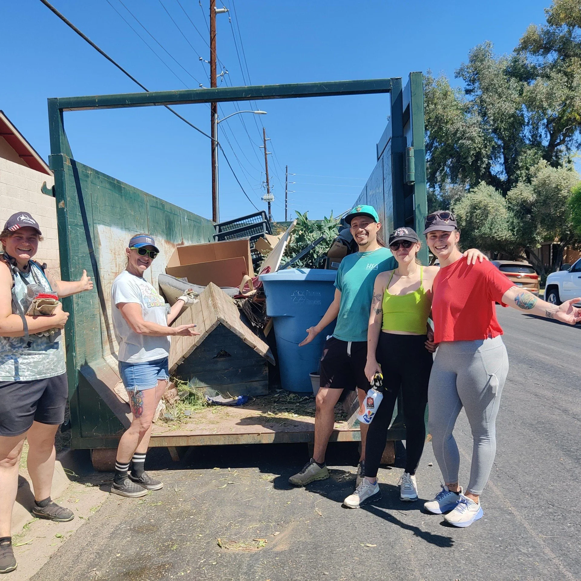 Group of people smiling and posing for a photo during a community cleanup event, standing near a truck filled with rubbish and reusable items.