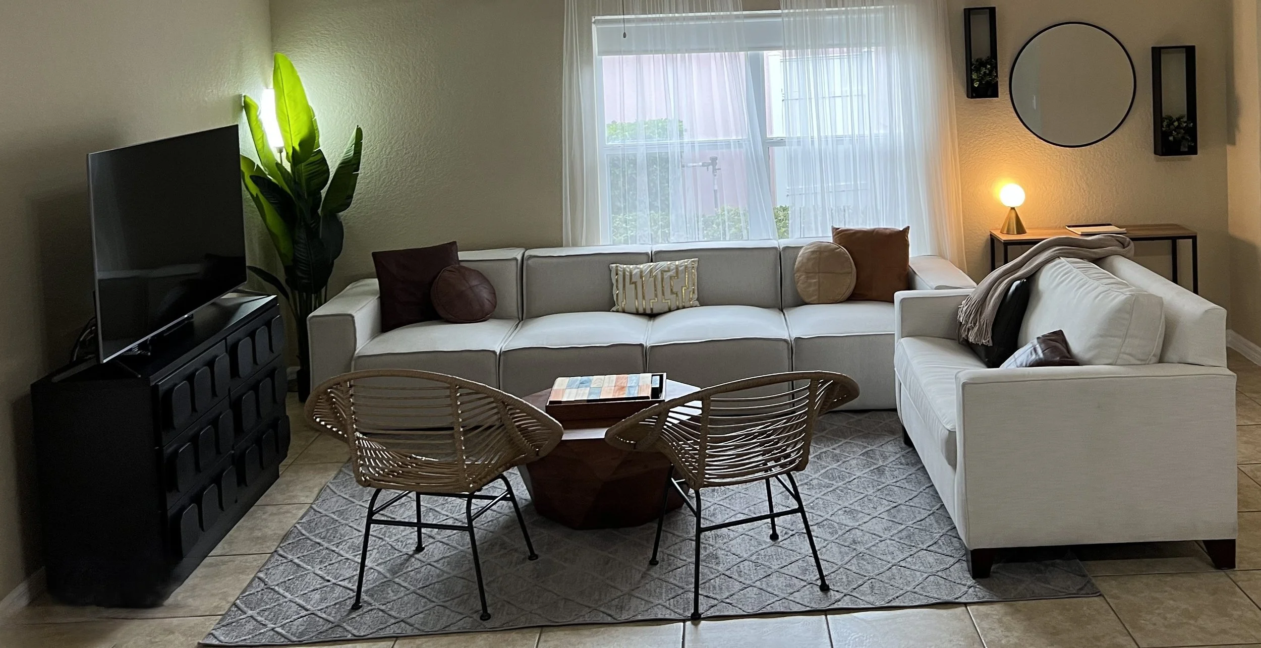 Cartoon woman with shoulder-length brown hair, glasses, gold hoop earrings, wearing a cream blouse with rolled-up sleeves and pink pants, smiling with one hand in her pocket.