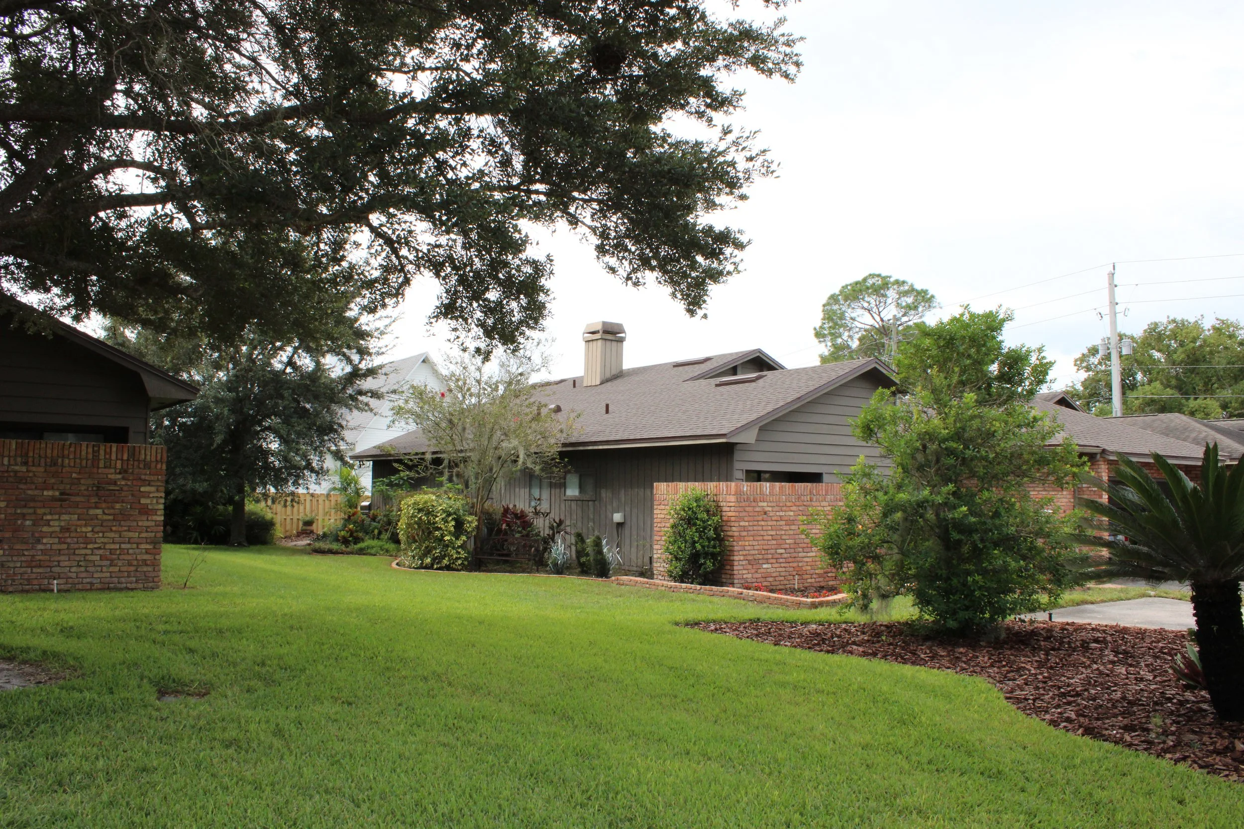 Modern small house with wooden exterior, large front window reflecting two people, set against a mountainous landscape with dry grass in the foreground.