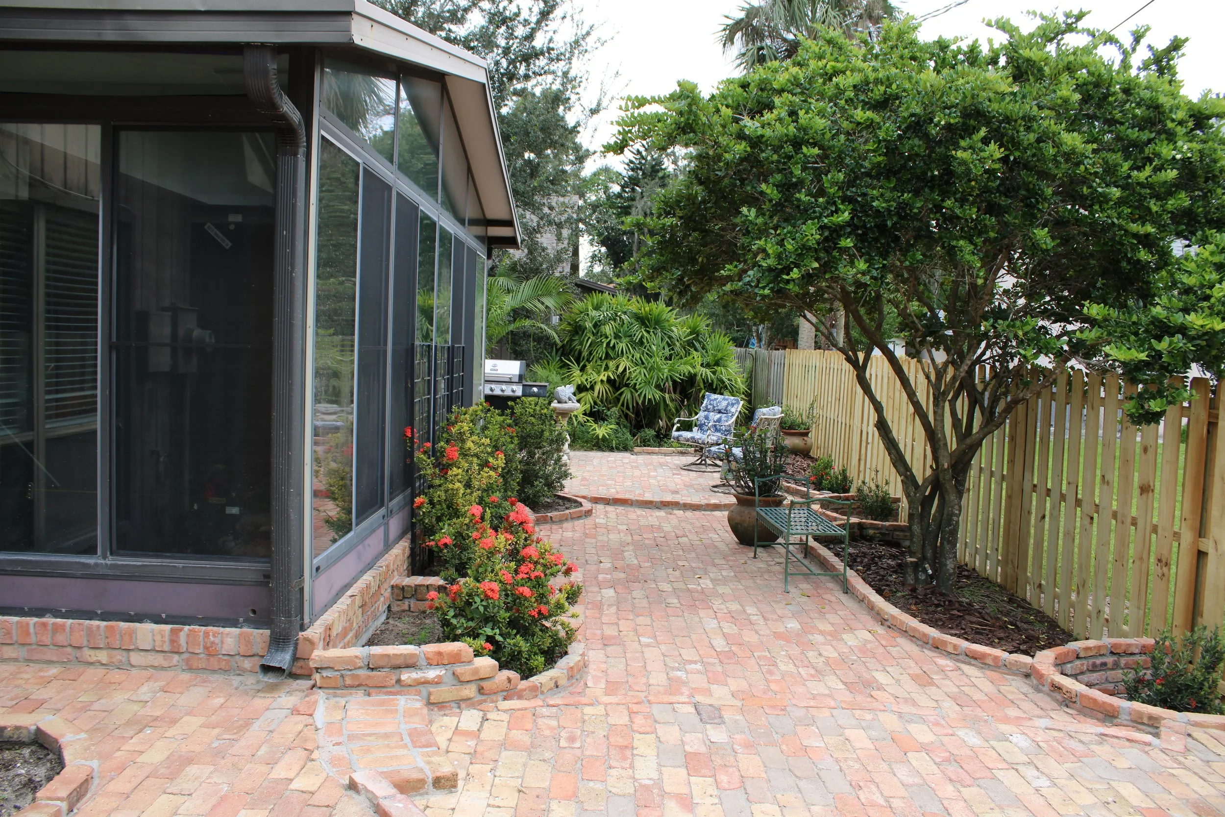 A modern wooden house with a sloped roof in a field of tall grass, overlooking a lake with mountains in the background during sunset.