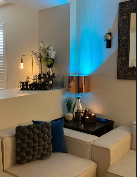 A cartoon woman with shoulder-length brown hair, glasses, and earrings, wearing a cream-colored blouse and pink pants, smiling with one hand in her pocket.