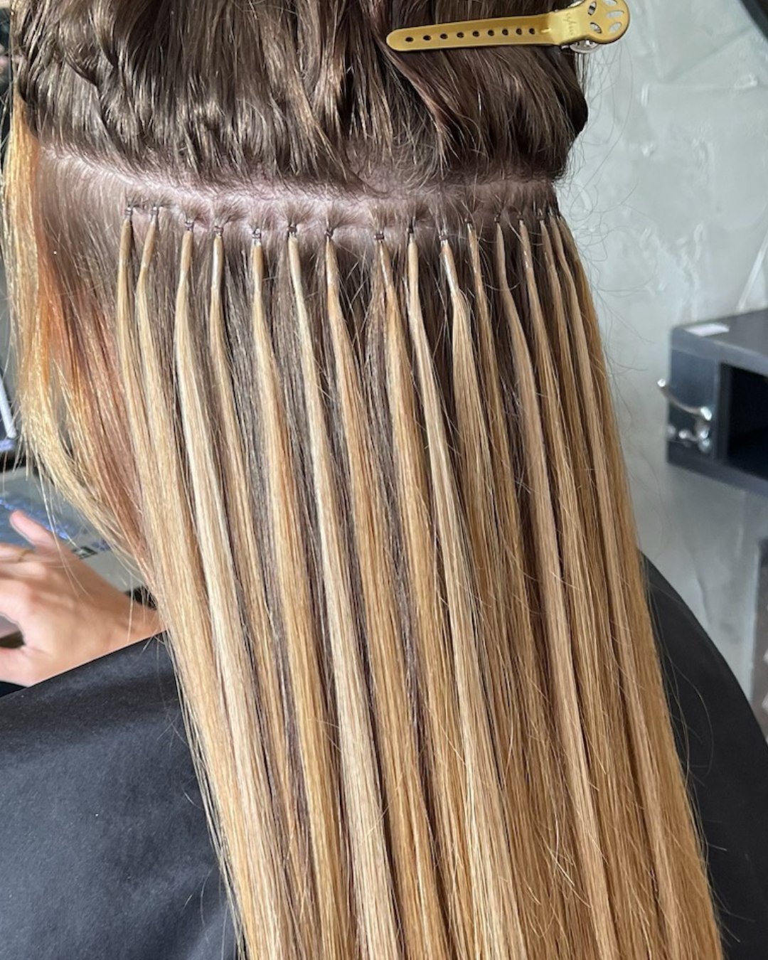 A person with long, blonde hair getting a hair highlighting treatment, with hair sections separated and pinned back, and a yellow hair clip on top.