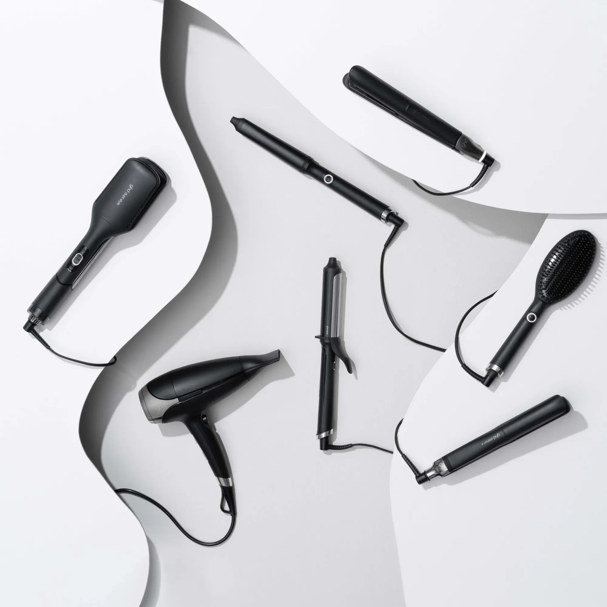 Collection of black hair styling tools on white background with curved paper and shadow effects.