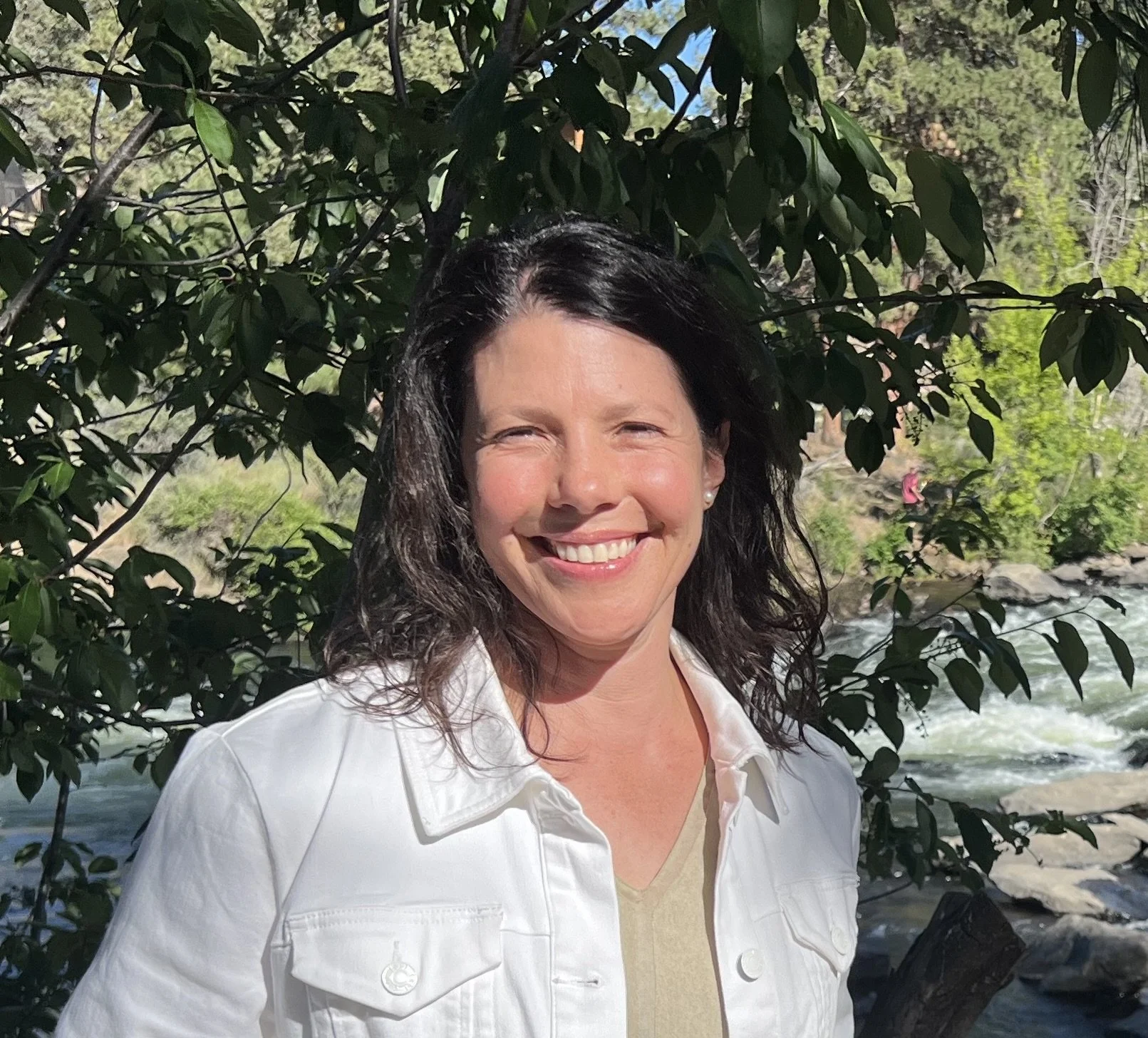 Woman with long brown hair smiling with trees in background