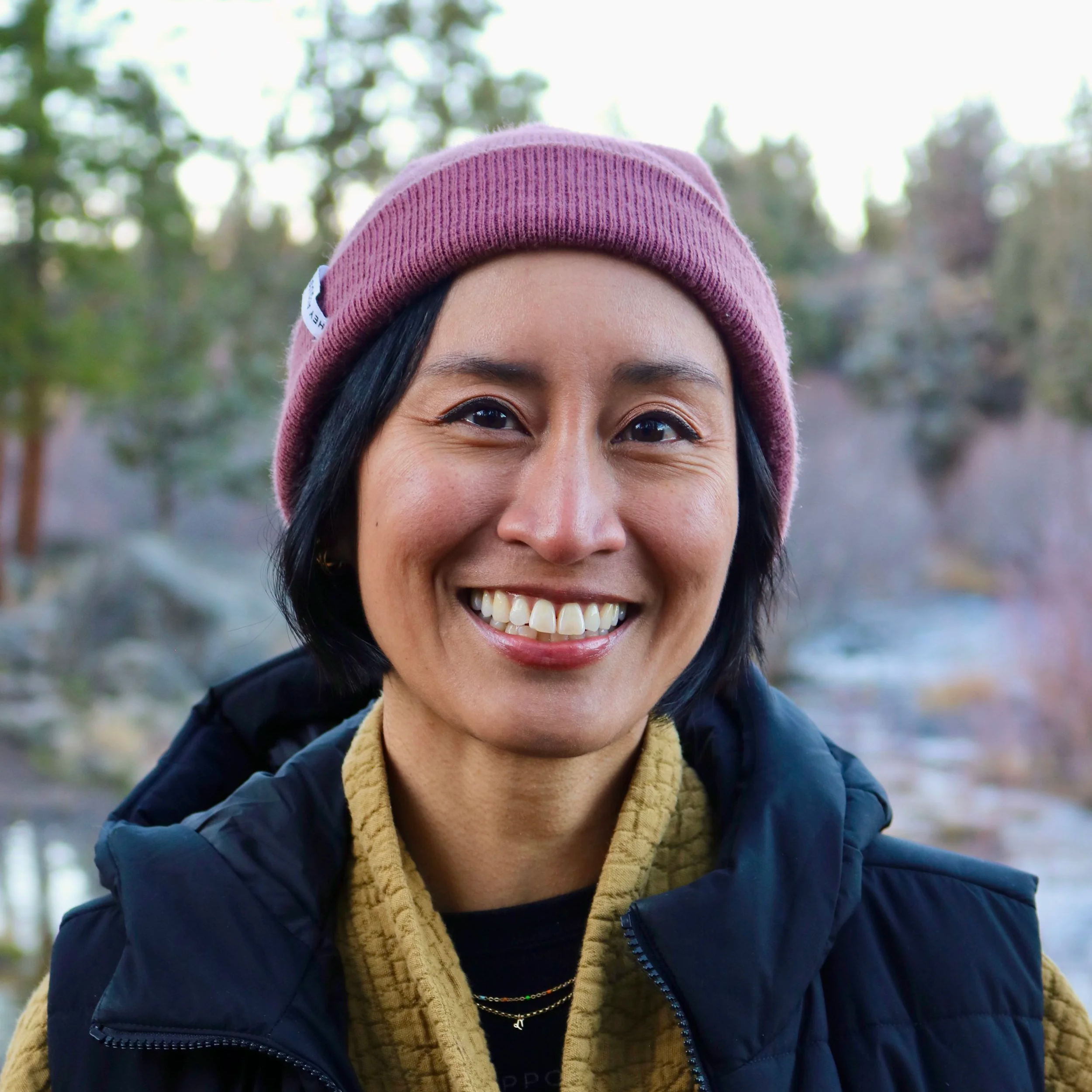 Smiling Filipino woman with brown skin, short black hair wearing a purple beanie