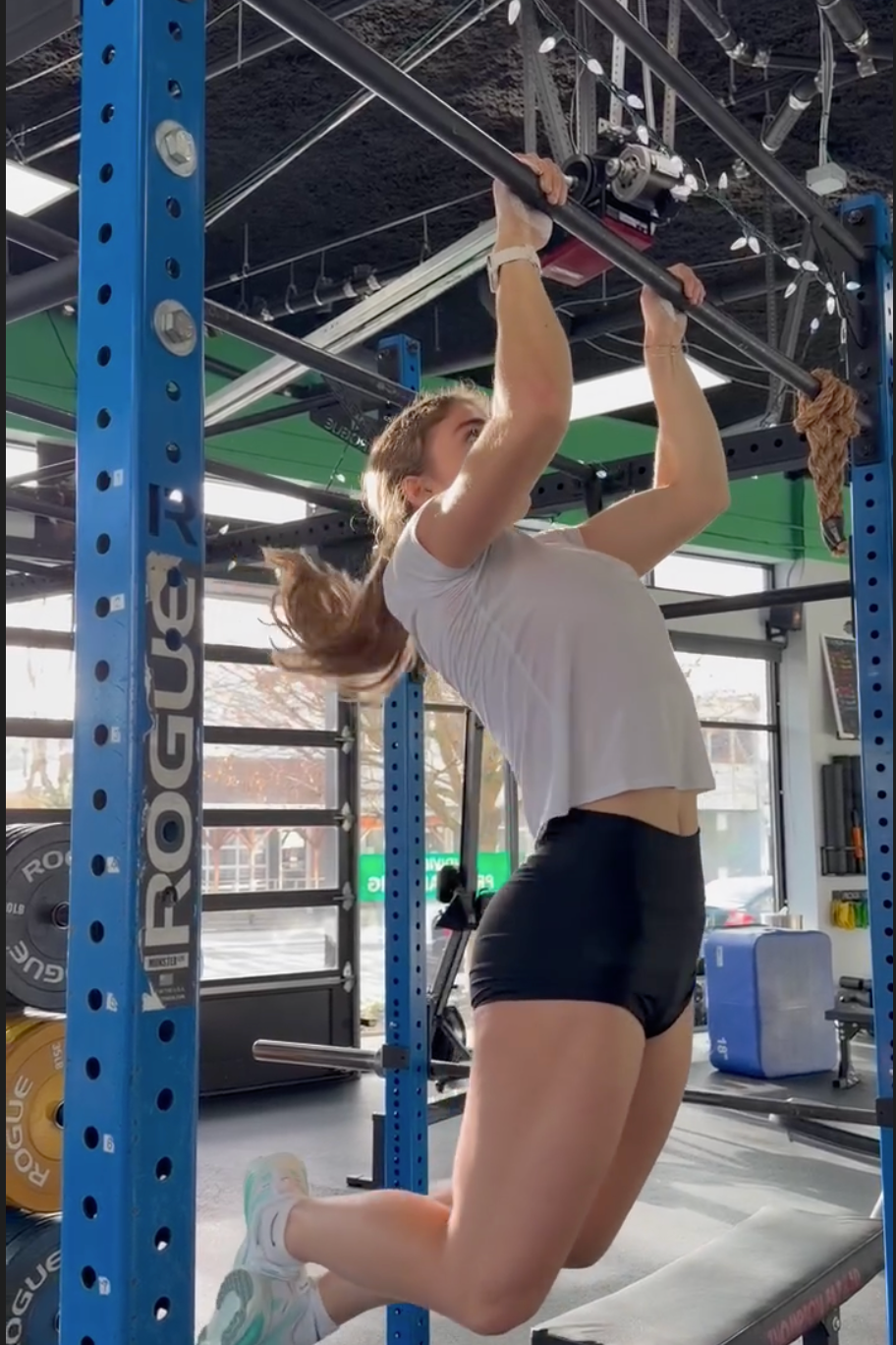 A seattle personal training client performs a pull-up exercise in NW Fitness Project, hanging from a black pull-up bar attached to a blue Rogue Fitness power rack.